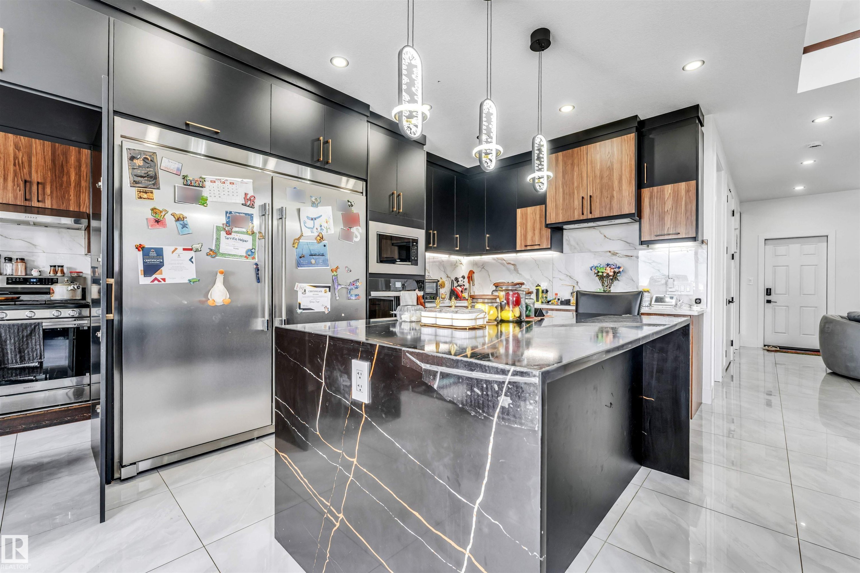 Gourmet kitchen featuring a large waterfall island with veined dark stone, stainless steel appliances, two-tone cabinetry, marble-look backsplash, and recessed lighting - 208 33 Street, Edmonton, AB