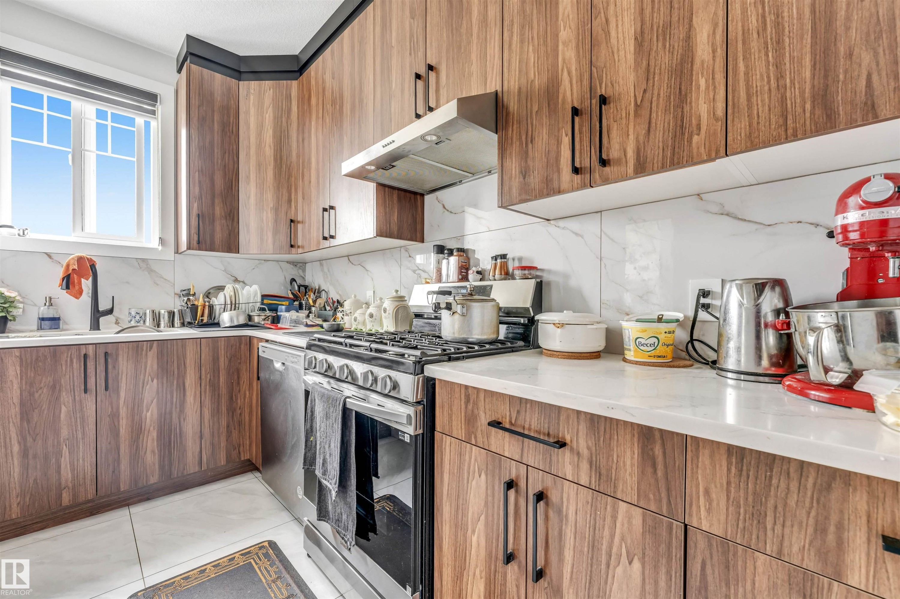 Kitchen featuring wood-finish cabinetry with matte black hardware, white countertop surfaces, and a full tile backsplash - 208 33 Street, Edmonton, AB