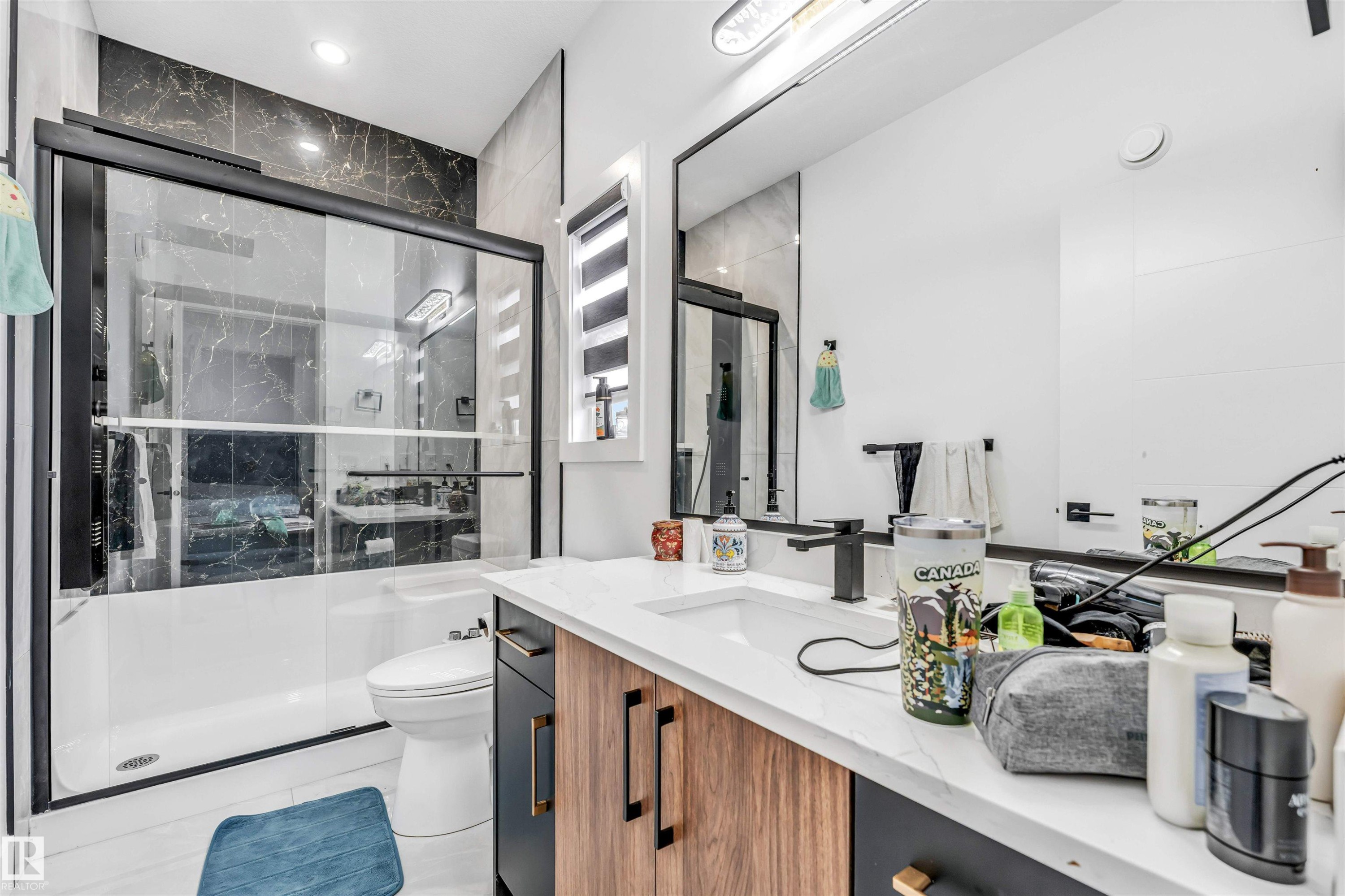 Contemporary bathroom featuring a black-framed glass sliding shower door over a white tub - 208 33 Street, Edmonton, AB