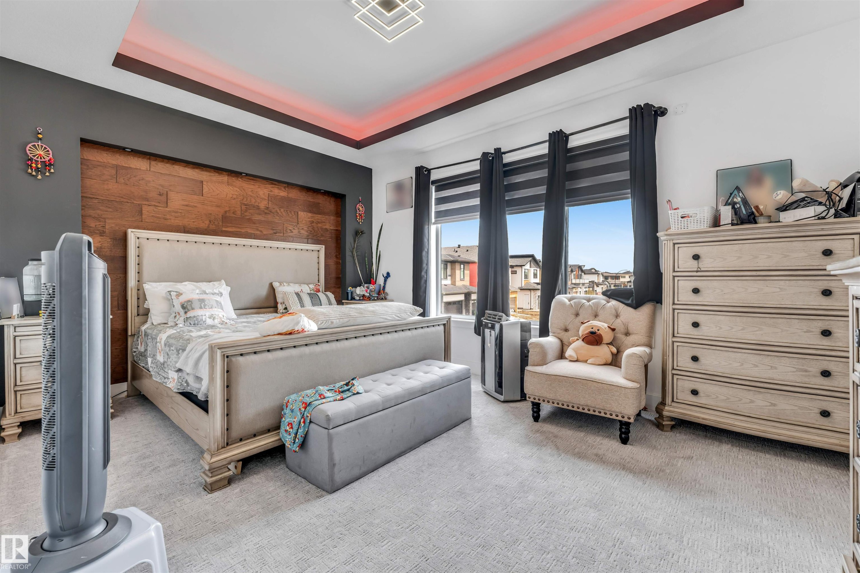 Recessed tray ceiling with accent lighting, wood-paneled feature wall, large windows with roller shades, and light-toned carpet - 208 33 Street, Edmonton, AB