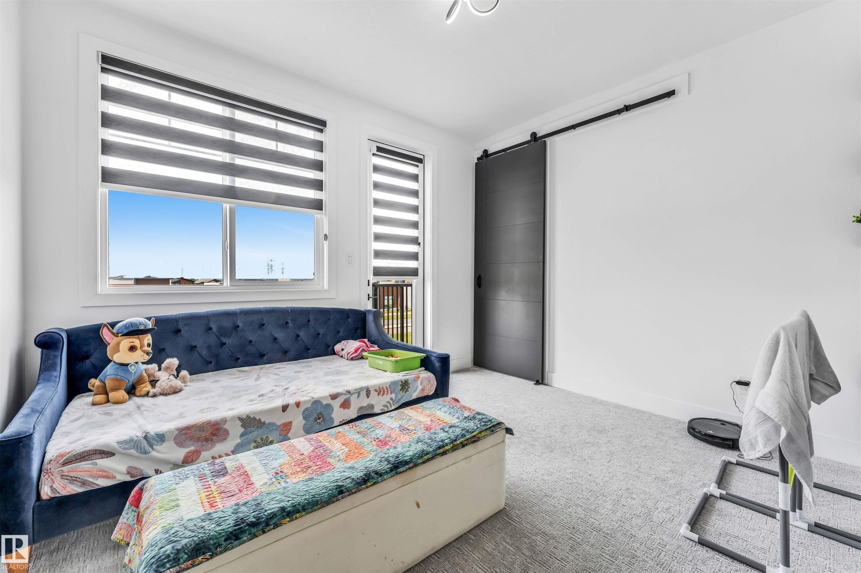 Bright interior space featuring a sliding barn door with black hardware, white walls, and light-toned carpeting - 208 33 Street, Edmonton, AB