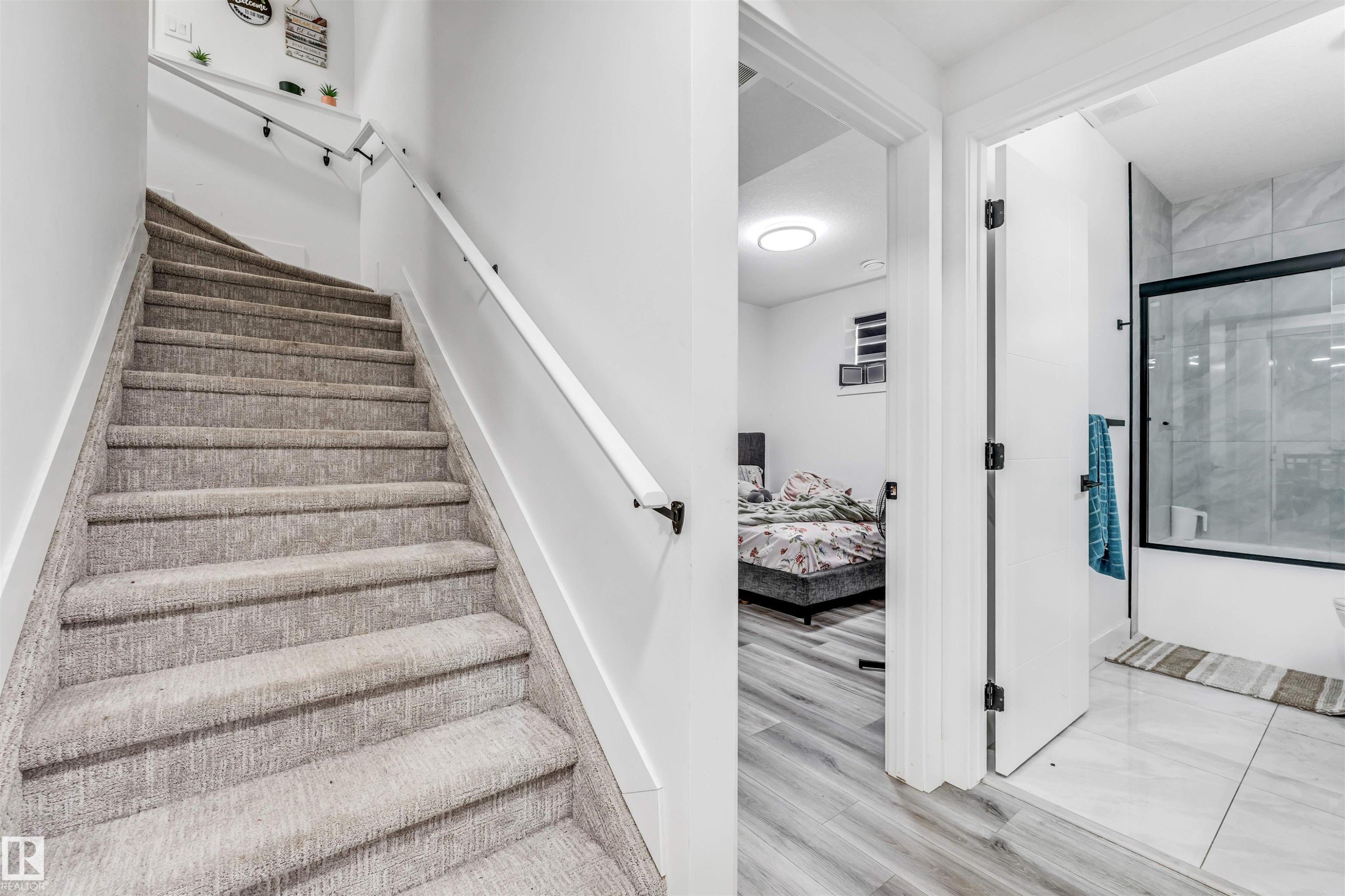 Carpeted staircase with white handrail, featuring a nearby bedroom with wood-finish flooring and a bathroom with a glass-enclosed tub/shower and large format tile flooring - 208 33 Street, Edmonton, AB