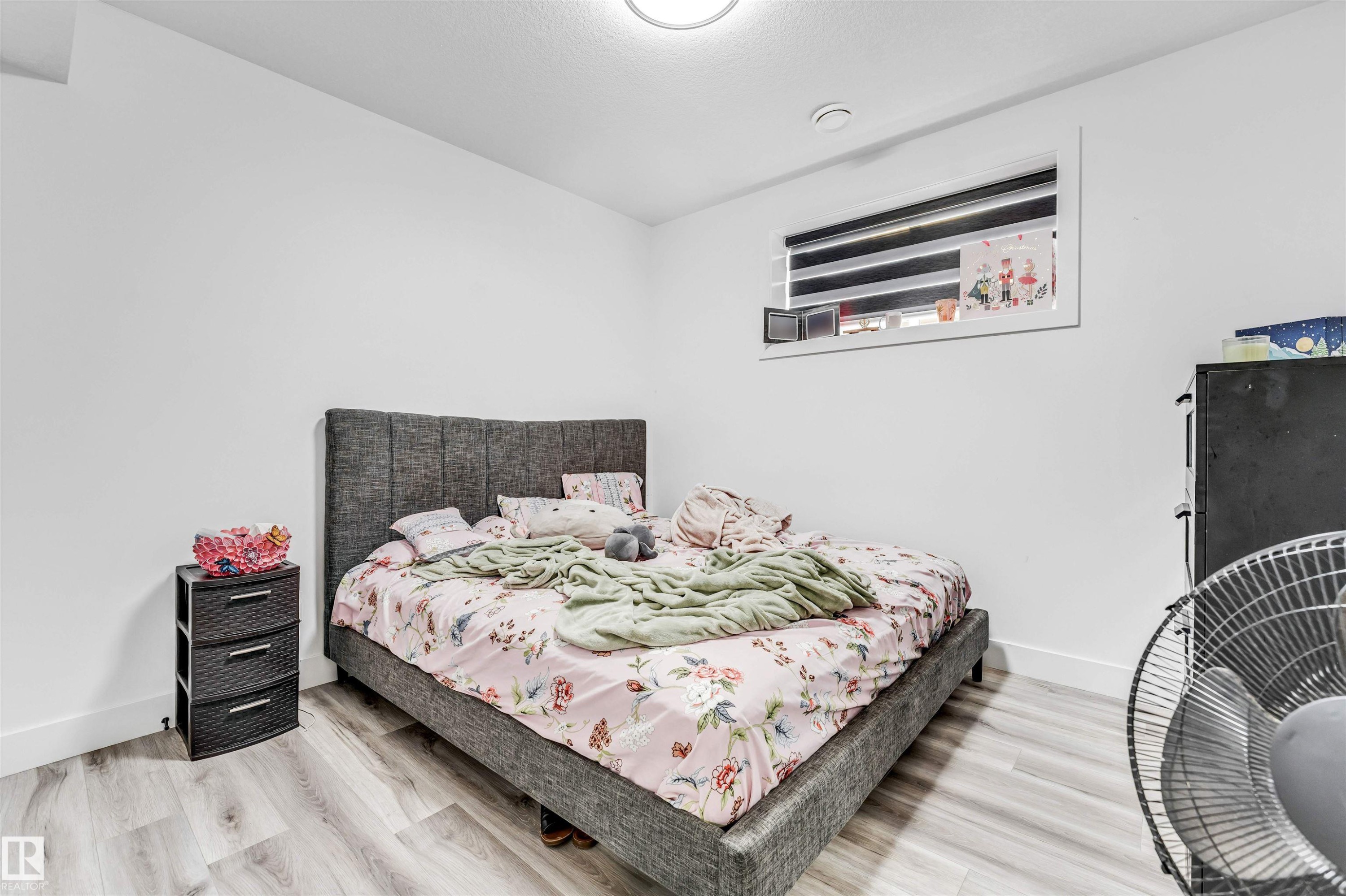 Bright room featuring light-toned wood-finish flooring, white painted walls, and a single window with horizontal blinds - 208 33 Street, Edmonton, AB