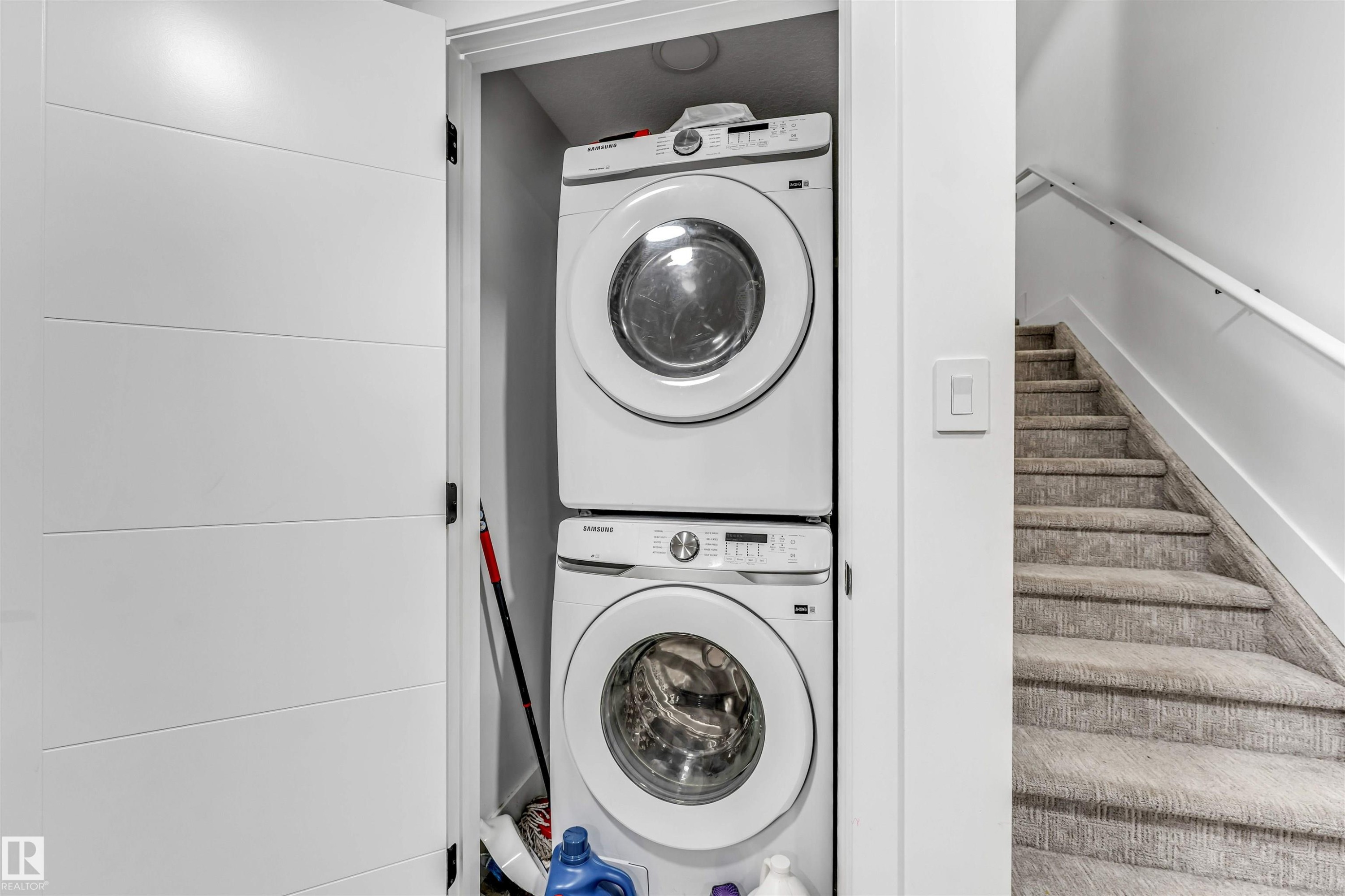 Dedicated laundry closet featuring a stackable washer and dryer, adjacent to a carpeted staircase with a white handrail - 208 33 Street, Edmonton, AB
