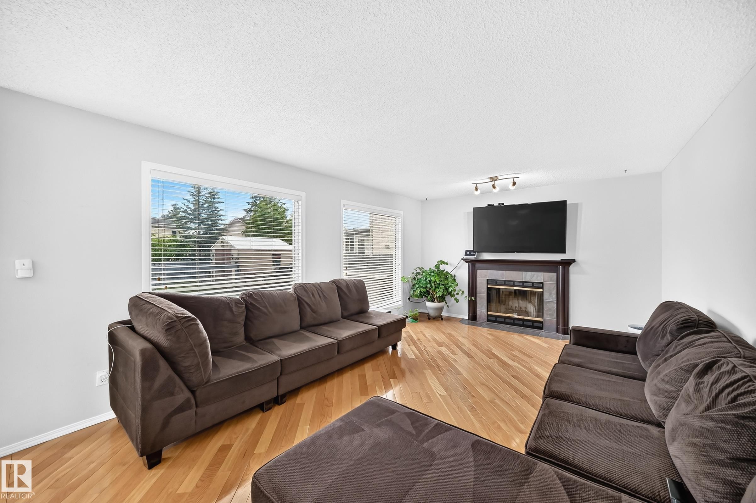 Living area featuring wood-finish flooring, multiple windows providing natural light, and a fireplace with a tile surround and dark wood mantel - 4216 47 Street, Edmonton, AB