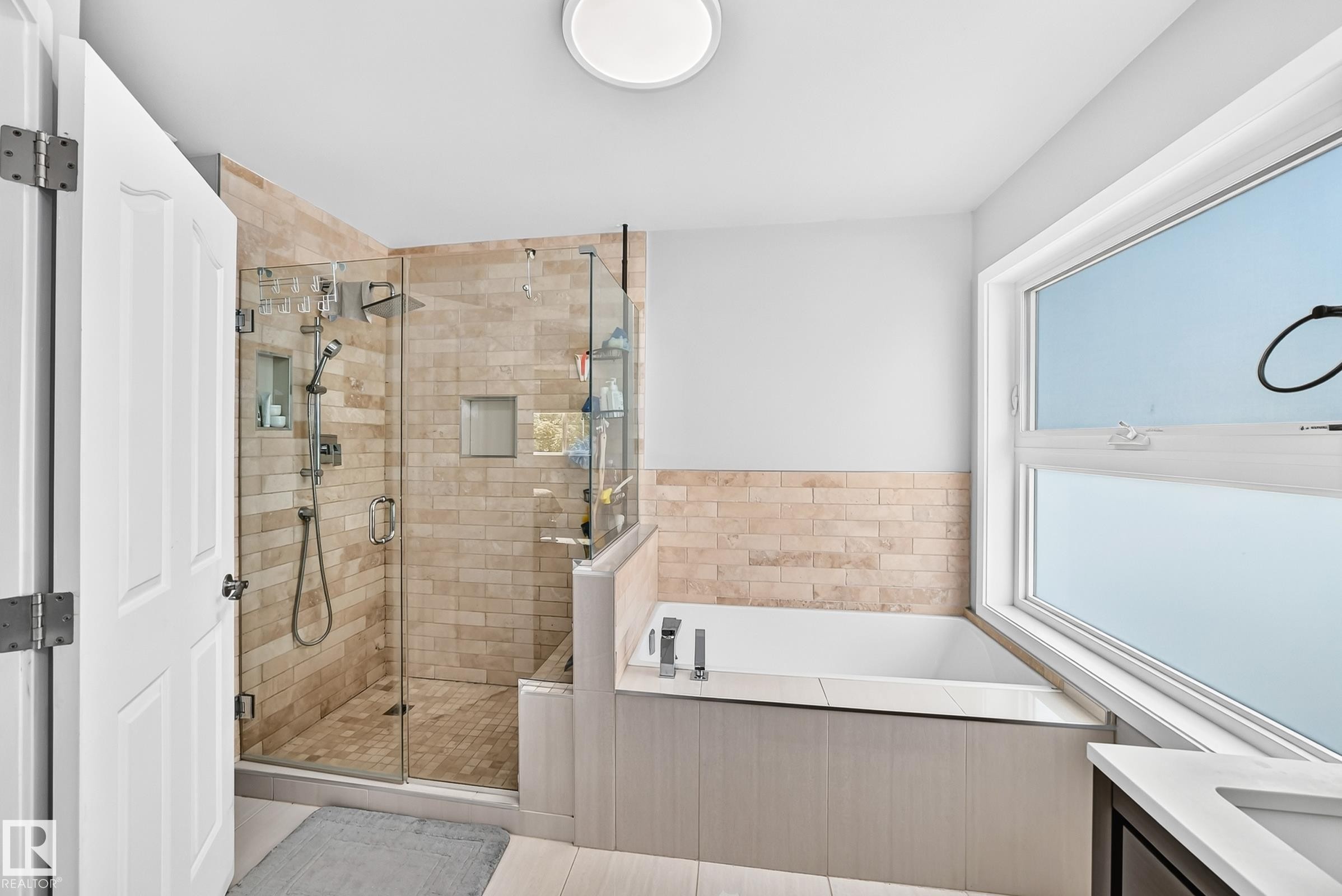 Bathroom featuring a glass-enclosed shower with tile surround, a built-in tub with paneling, and a large window - 4216 47 Street, Edmonton, AB