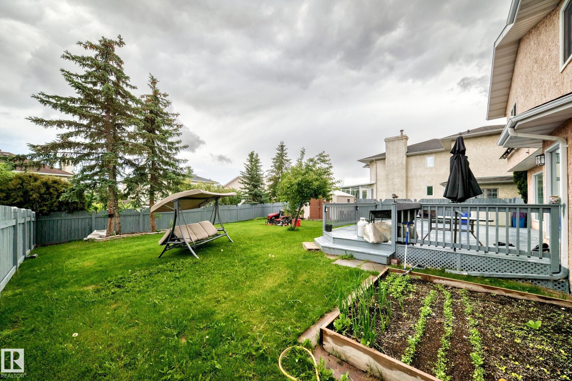 Expansive backyard featuring a multi-level deck, perimeter fencing, mature evergreen trees, and a raised garden bed - 4216 47 Street, Edmonton, AB