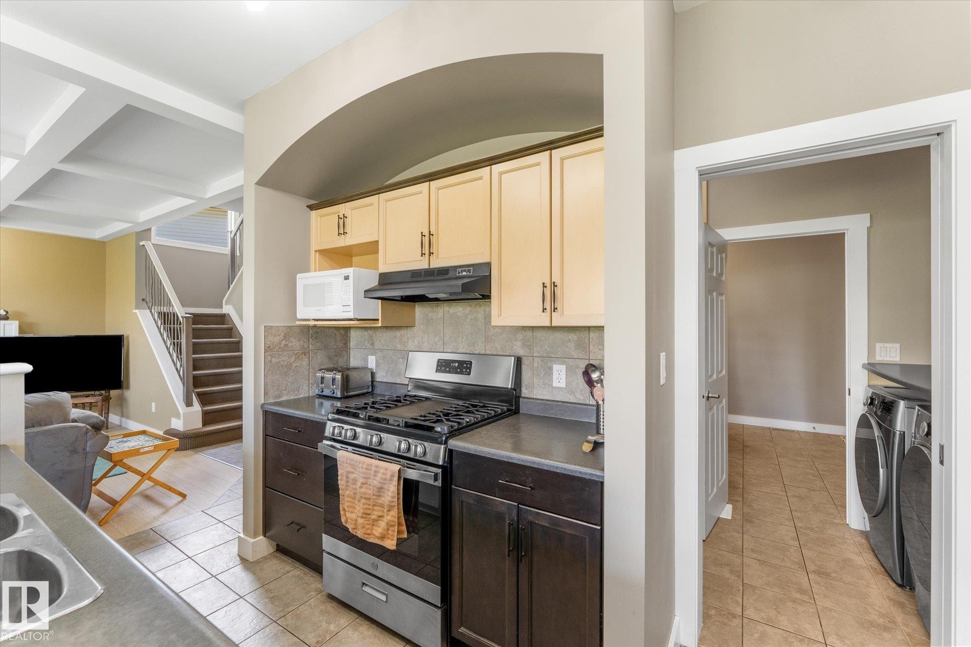 Kitchen featuring light wood-finish upper cabinetry, dark wood-finish lower cabinetry, and a stainless steel gas range - 488 Macewan Road, Edmonton, AB