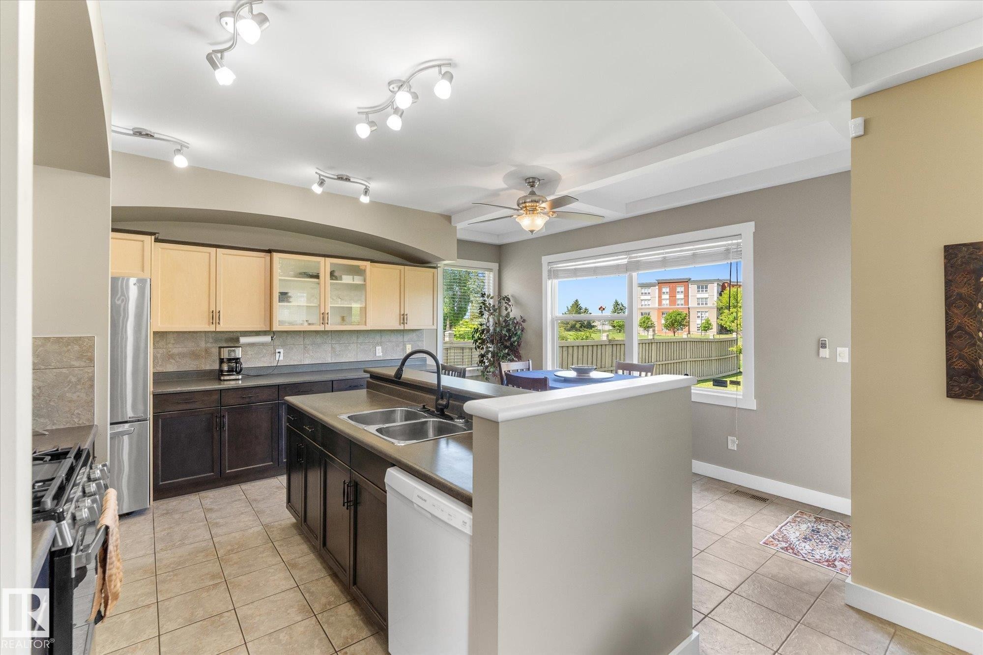 Spacious kitchen featuring an expansive island with dual basin sink, light and dark wood-finish cabinetry, tile flooring, and track lighting - 488 Macewan Road, Edmonton, AB