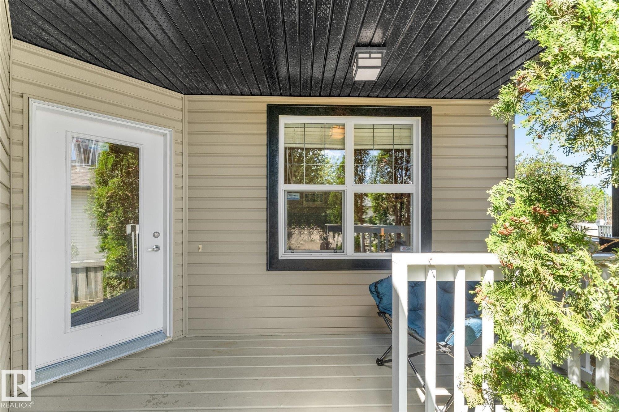 Covered porch entry featuring a full-light door, horizontal siding, and a dark-stained wood ceiling with an exterior light fixture - 488 Macewan Road, Edmonton, AB