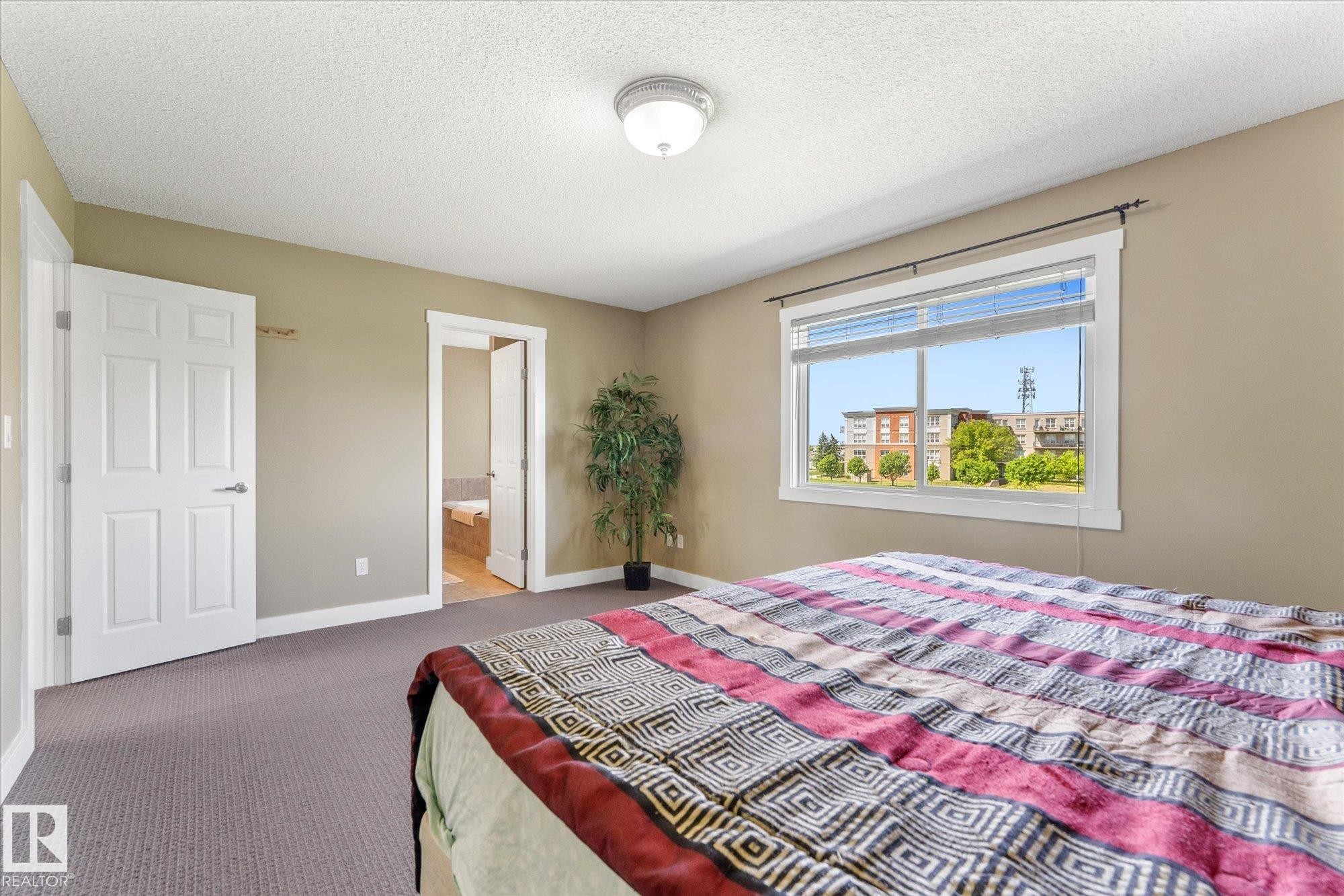 Spacious bedroom featuring neutral wall paint, white trim, and a window offering natural light - 488 Macewan Road, Edmonton, AB
