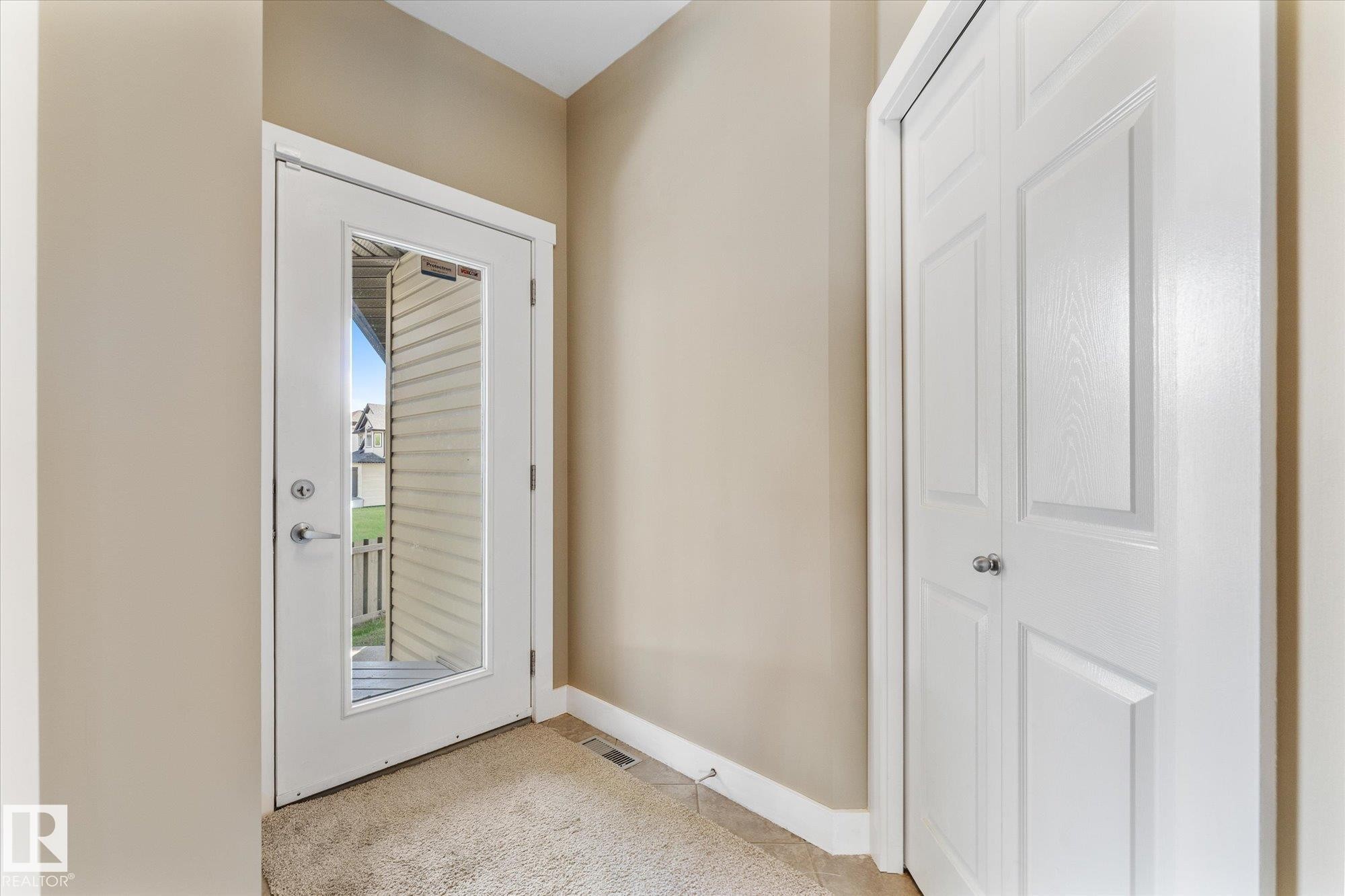 Entryway featuring a full-light exterior door with clear glass, a paneled bi-fold closet door, and a combination of carpet and tile flooring - 488 Macewan Road, Edmonton, AB