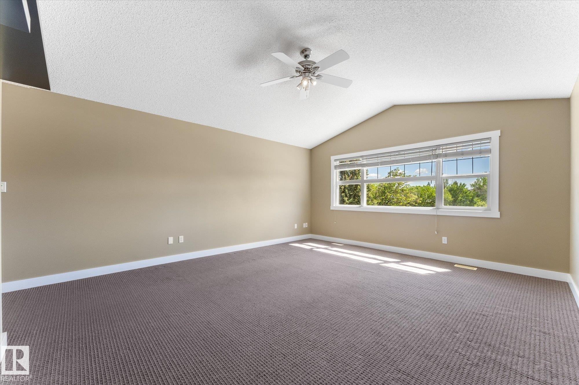 Room featuring a vaulted ceiling with a ceiling fan, a large window with blinds, and neutral-toned carpeting - 488 Macewan Road, Edmonton, AB