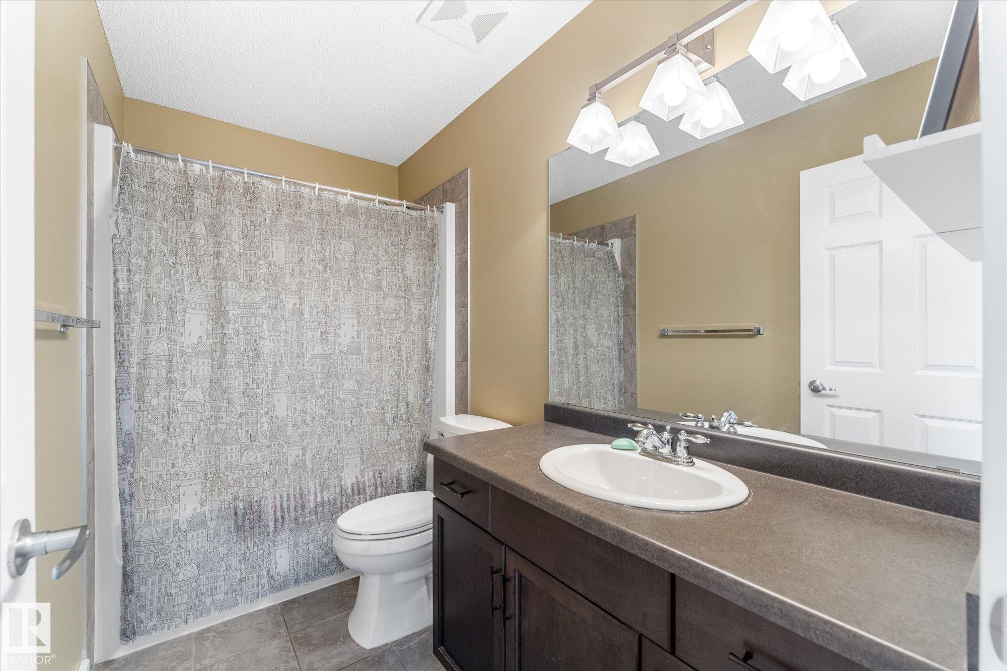 Bathroom featuring a dark wood-finish vanity with an integrated sink, a large mirror, and a four-light vanity fixture - 488 Macewan Road, Edmonton, AB