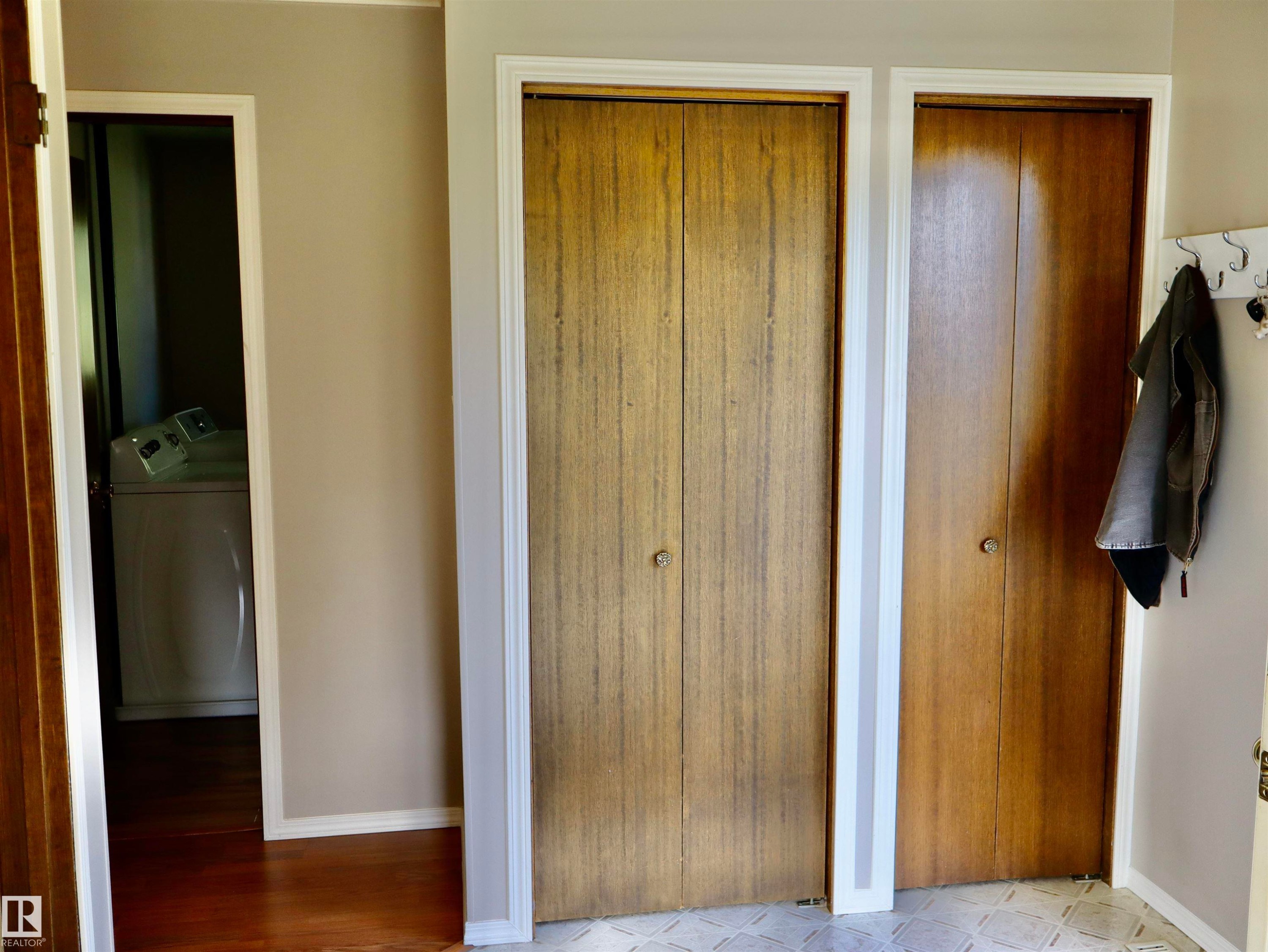 Wood-finish bi-fold closet doors with round knobs, white trim, and a patterned floor tile - 5530 46 Street, Barrhead, AB