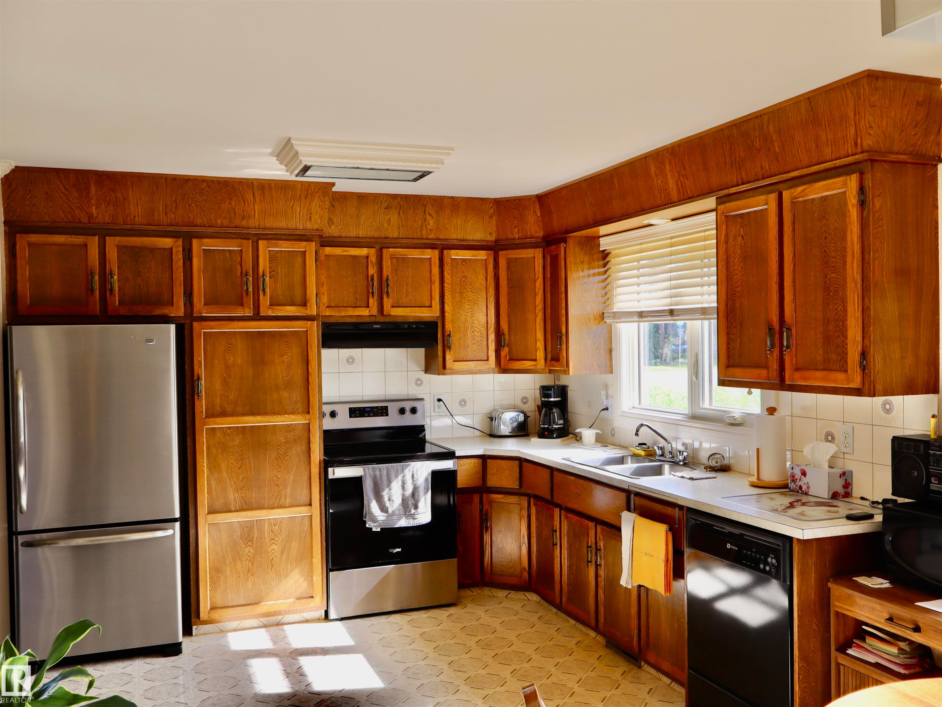 Kitchen featuring extensive wood cabinetry, white countertops, and a tile backsplash - 5530 46 Street, Barrhead, AB
