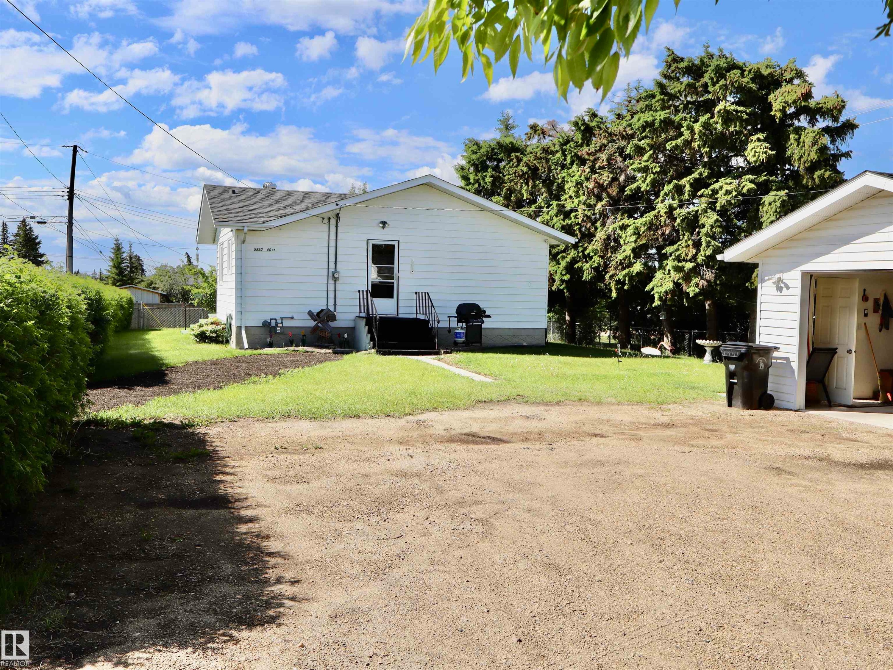 Backyard featuring a detached garage with an open bay, a gravel drive, and a manicured lawn - 5530 46 Street, Barrhead, AB