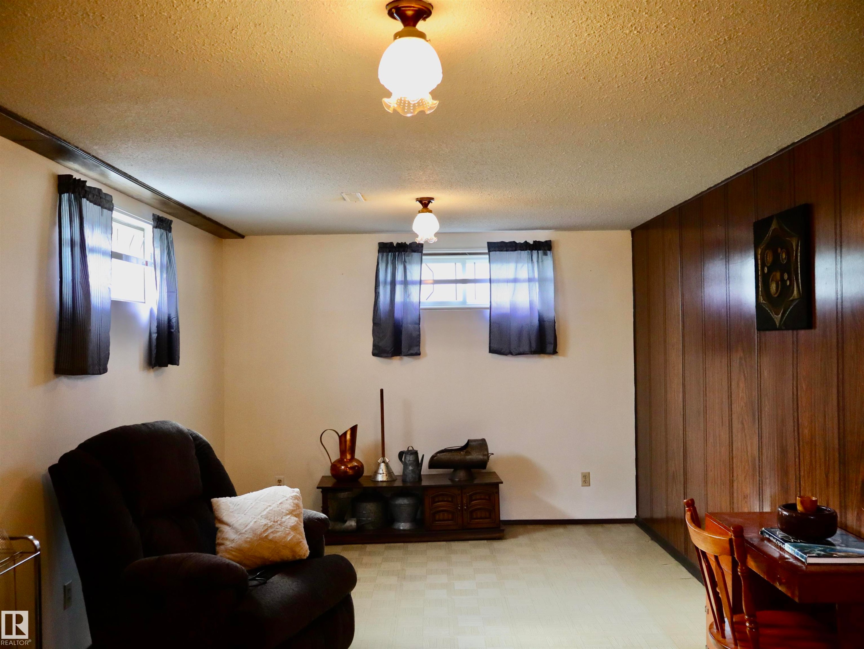 Room featuring wood paneling, light wall paint, checkerboard pattern flooring, and two ceiling-mounted light fixtures - 5530 46 Street, Barrhead, AB