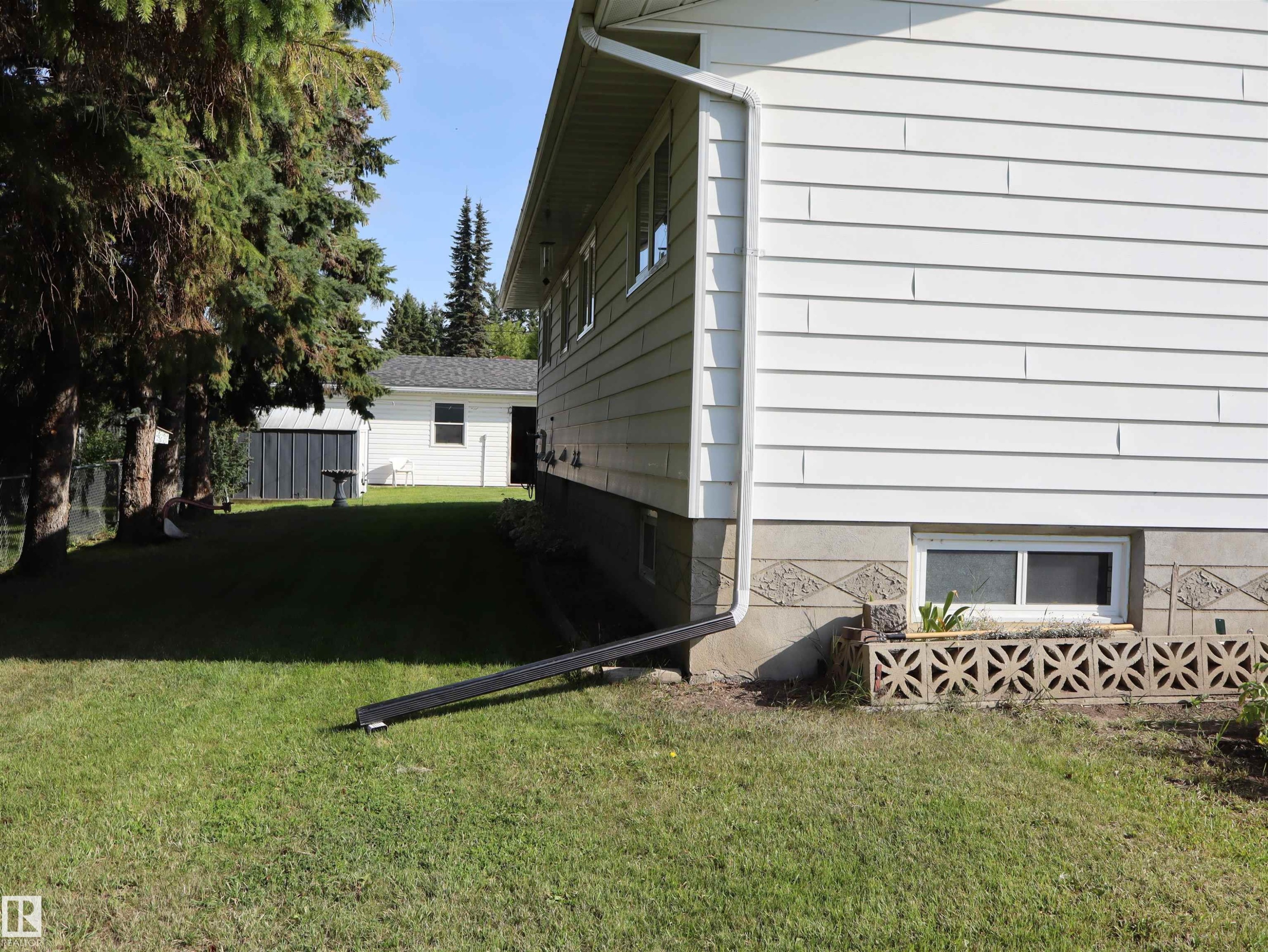 White horizontal siding, decorative concrete block foundation, and a white-framed basement window - 5530 46 Street, Barrhead, AB - Outdoor With Exterior