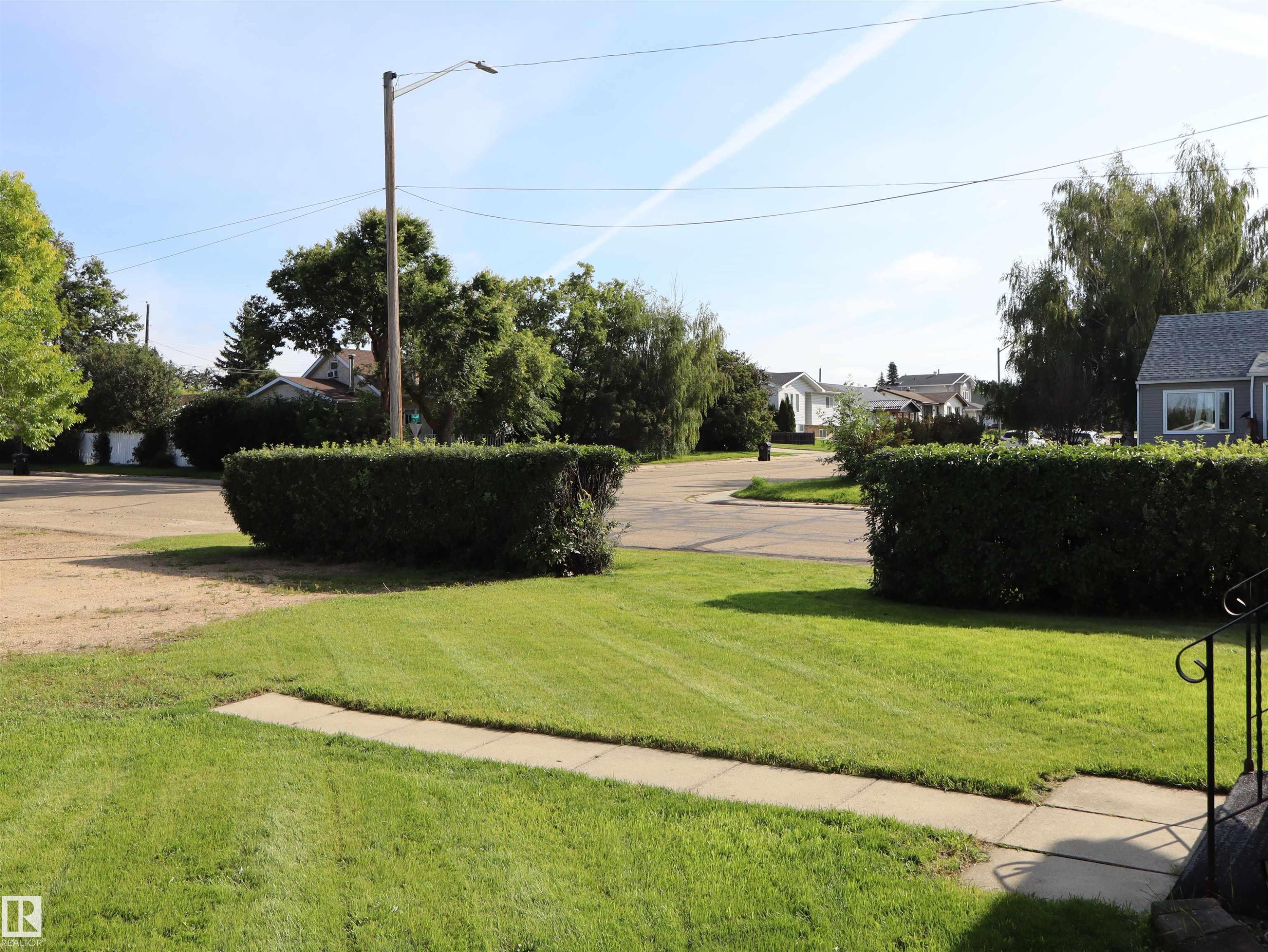 Manicured lawn with concrete pathway, surrounded by trimmed hedges and mature trees - 5530 46 Street, Barrhead, AB - Outdoor