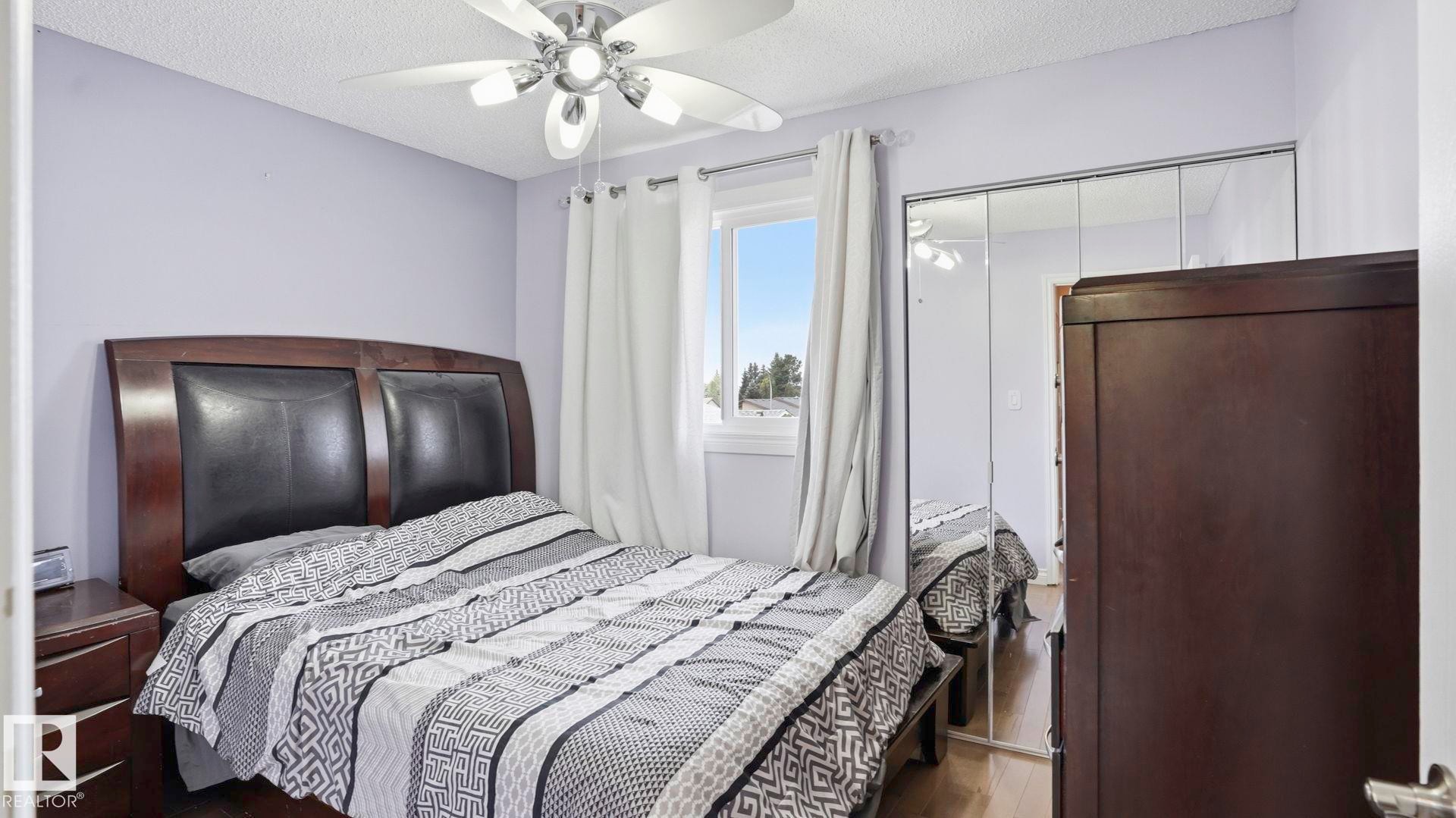 Bedroom featuring wood-finish flooring, a ceiling fan with integrated lighting, and mirrored closet doors - 1827 36 Street Nw, Edmonton, AB