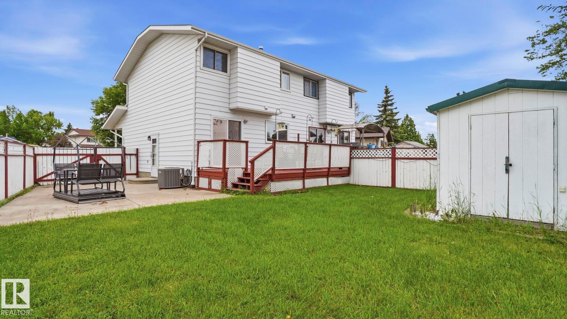 Spacious backyard featuring a large green lawn, a white exterior home with multiple windows, and a dedicated storage shed - 1827 36 Street Nw, Edmonton, AB