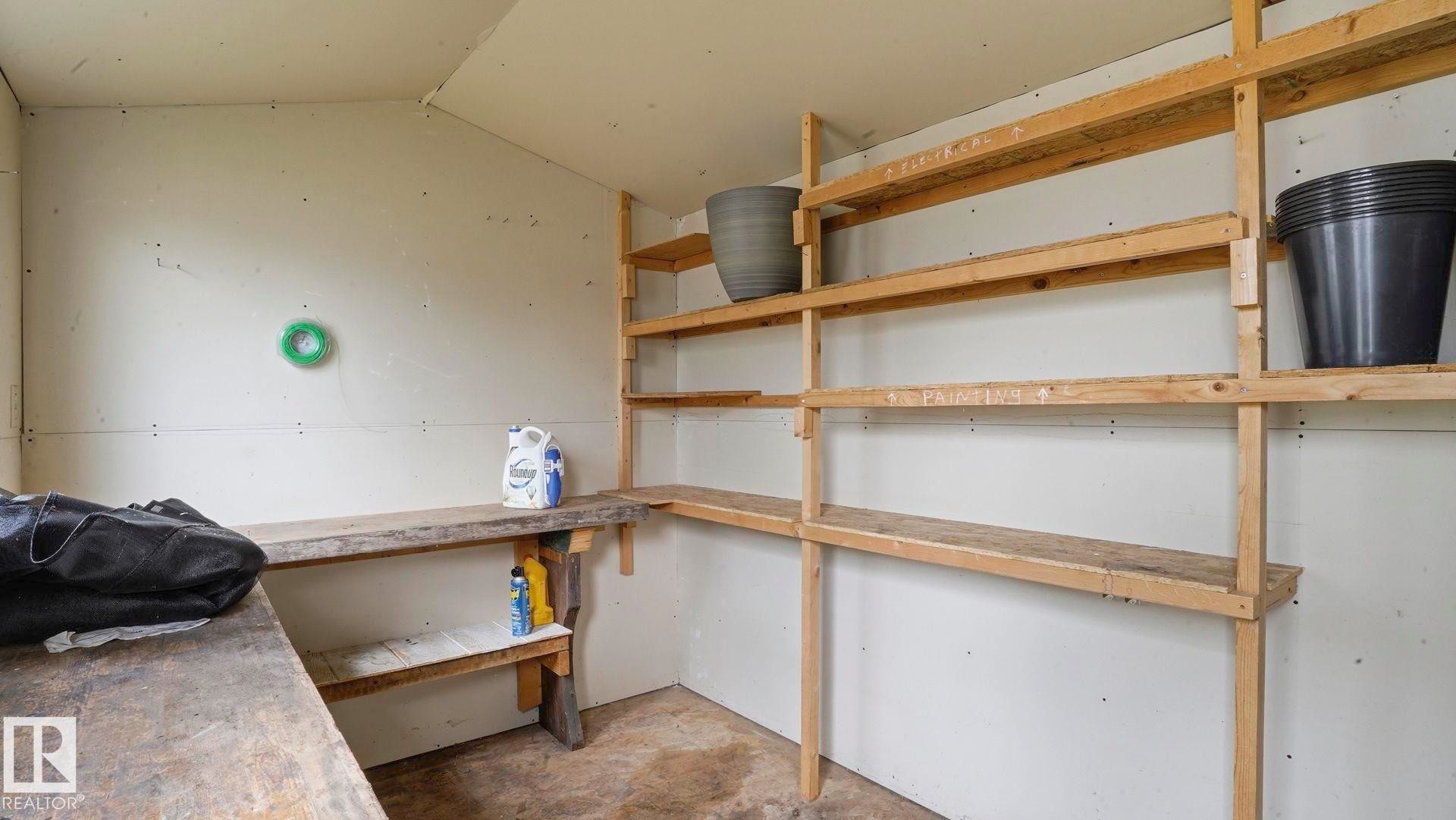 Utility room featuring extensive wood shelving, a built-in workbench, and concrete flooring - 1827 36 Street Nw, Edmonton, AB