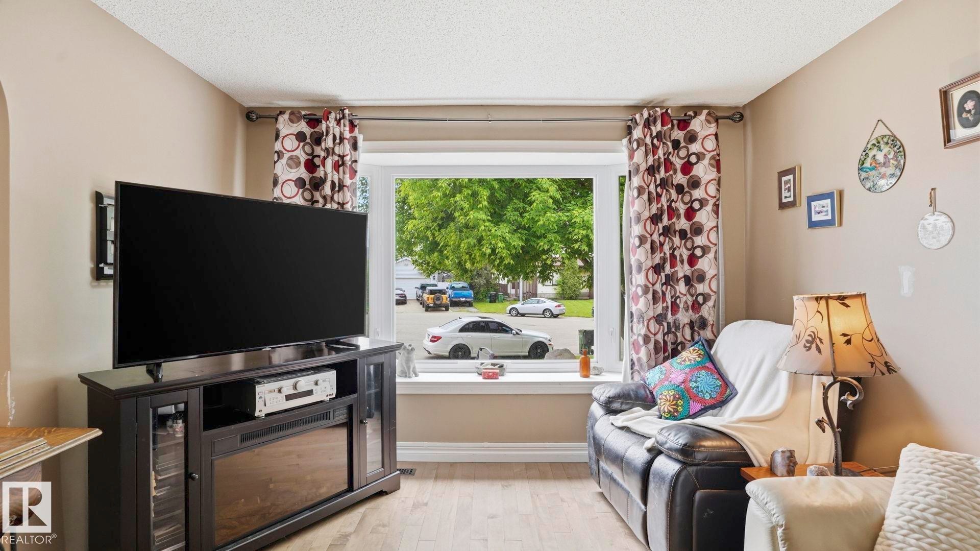 Living space featuring wood-finish flooring, a large window, and light-toned wall paint - 1827 36 Street Nw, Edmonton, AB