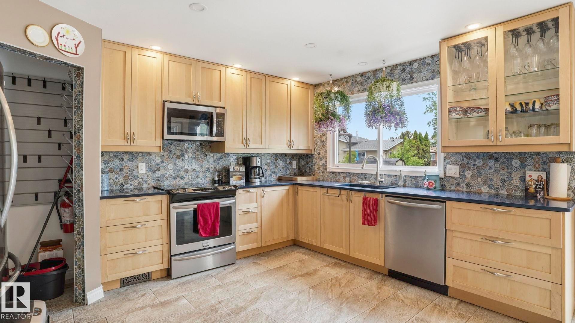 Kitchen featuring light wood cabinetry, stone countertops, and stainless steel appliances - 1827 36 Street Nw, Edmonton, AB