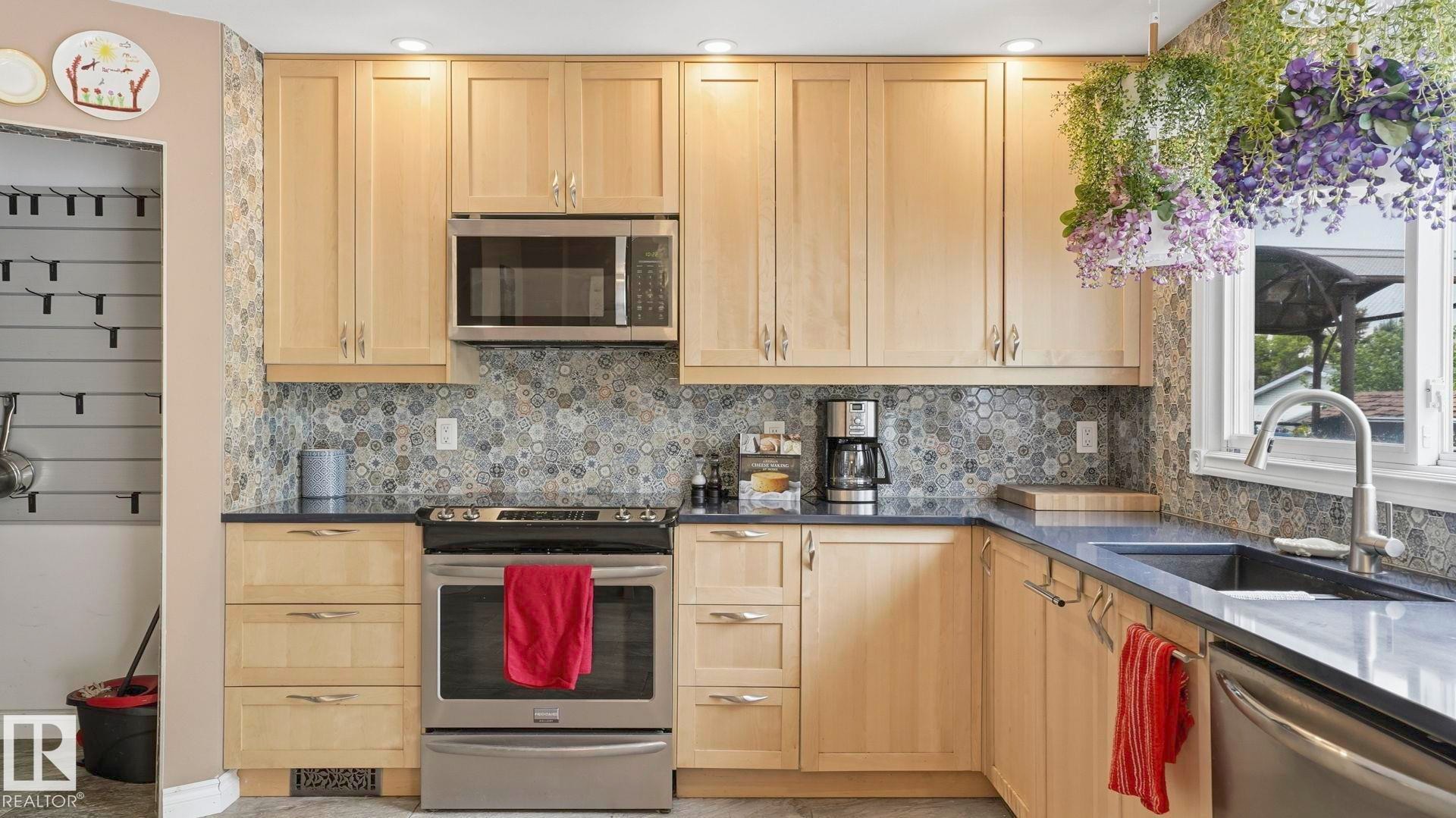 Kitchen featuring light wood cabinetry, stainless steel appliances, dark countertops, and a patterned tile backsplash - 1827 36 Street Nw, Edmonton, AB