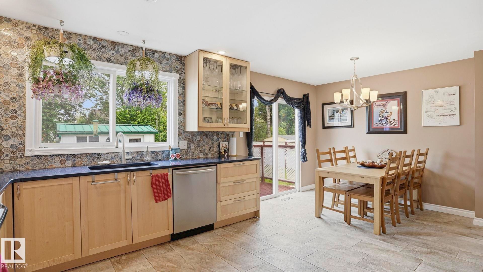 Kitchen featuring light wood cabinetry, a dark countertop, stainless steel appliances, and a patterned backsplash - 1827 36 Street Nw, Edmonton, AB