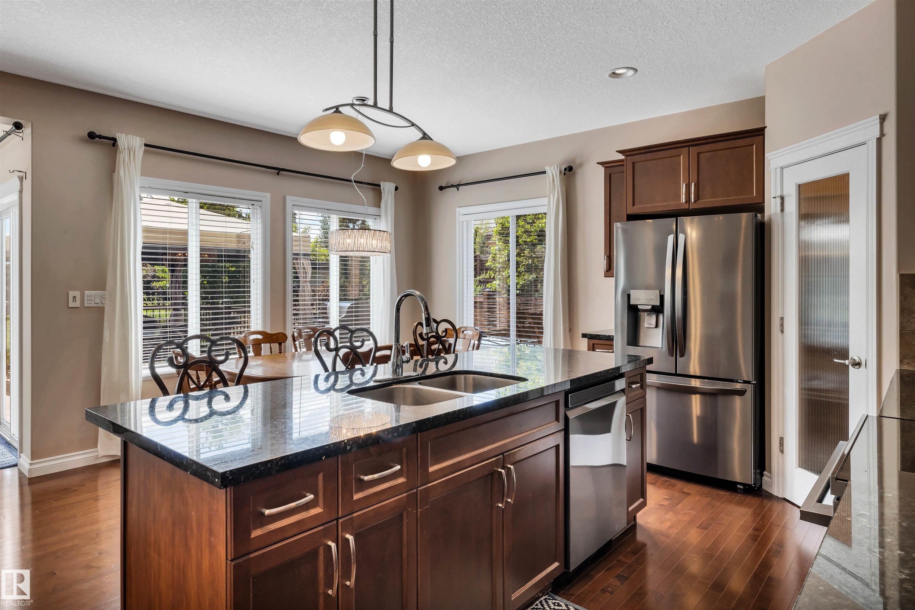 Kitchen featuring a central island with a dual-basin sink, dark stone-finish countertop, and wood-finish cabinetry - 18 Voleta Crest, Spruce Grove, AB