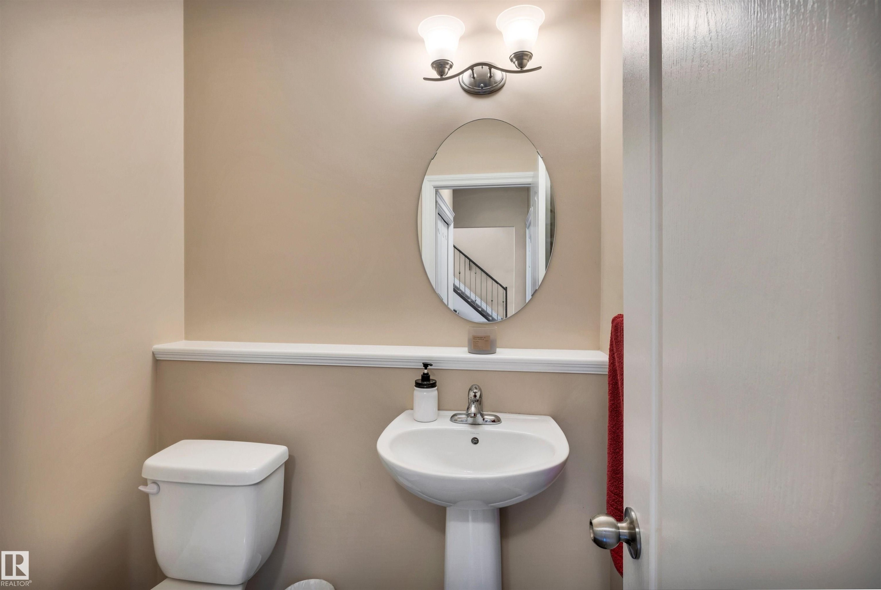 Powder room featuring a pedestal sink, oval mirror, and wall-mounted light fixture - 18 Voleta Crest, Spruce Grove, AB