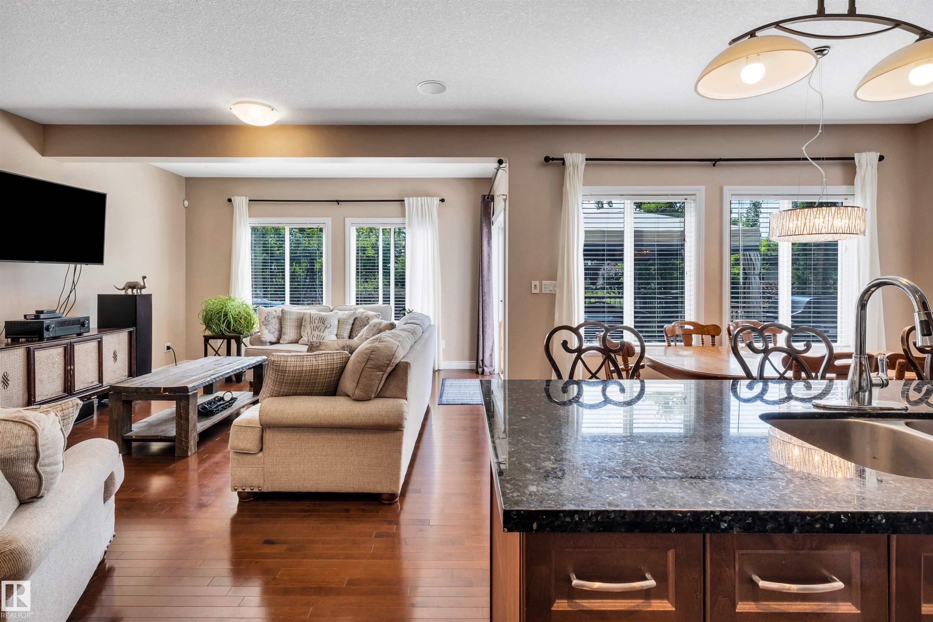 Kitchen with a dark granite countertop and stainless steel sink, overlooking a living area with wood-finish flooring - 18 Voleta Crest, Spruce Grove, AB