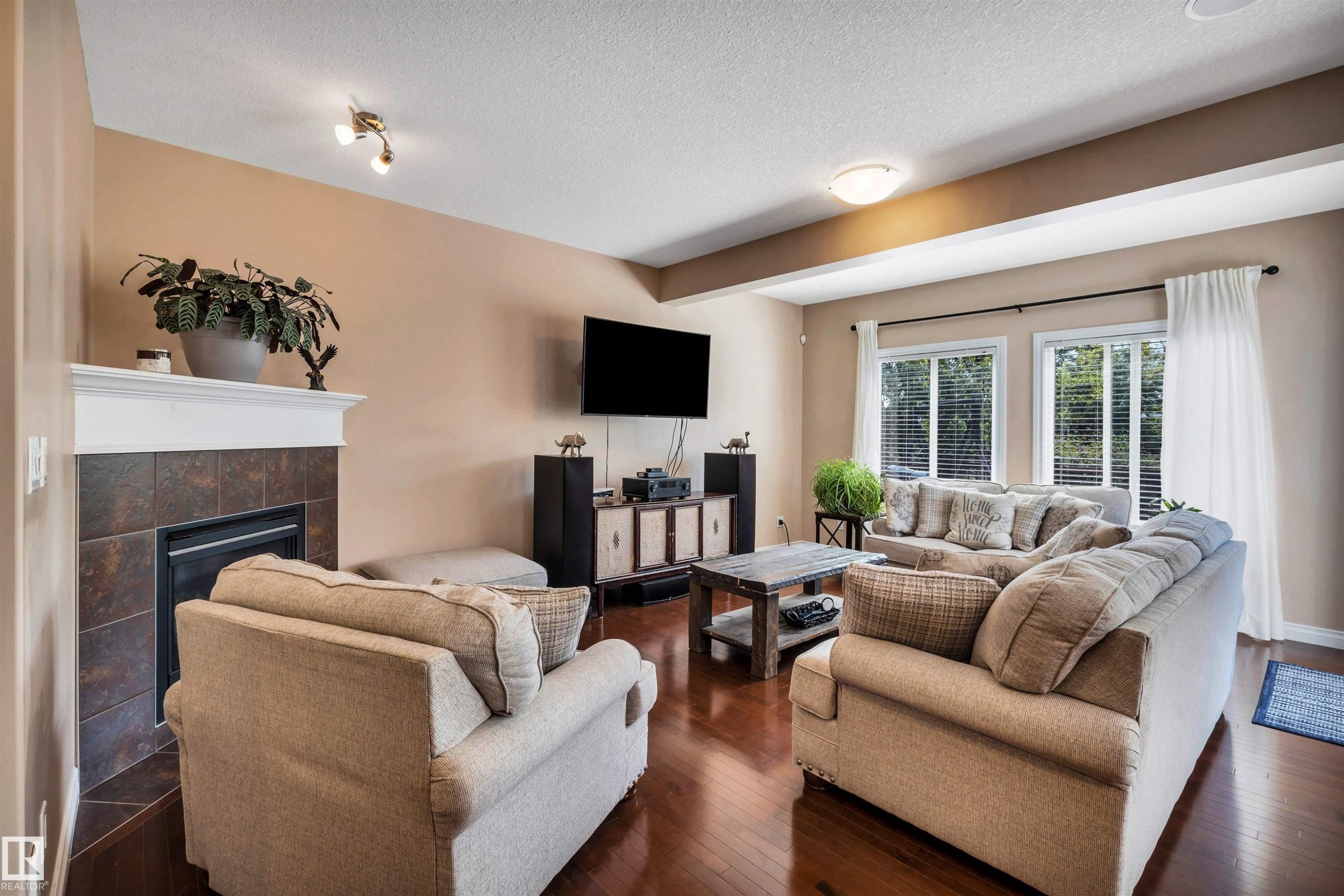Living area featuring rich wood-finish flooring, a built-in fireplace with tile surround and white mantel, and ample natural light through multiple windows - 18 Voleta Crest, Spruce Grove, AB
