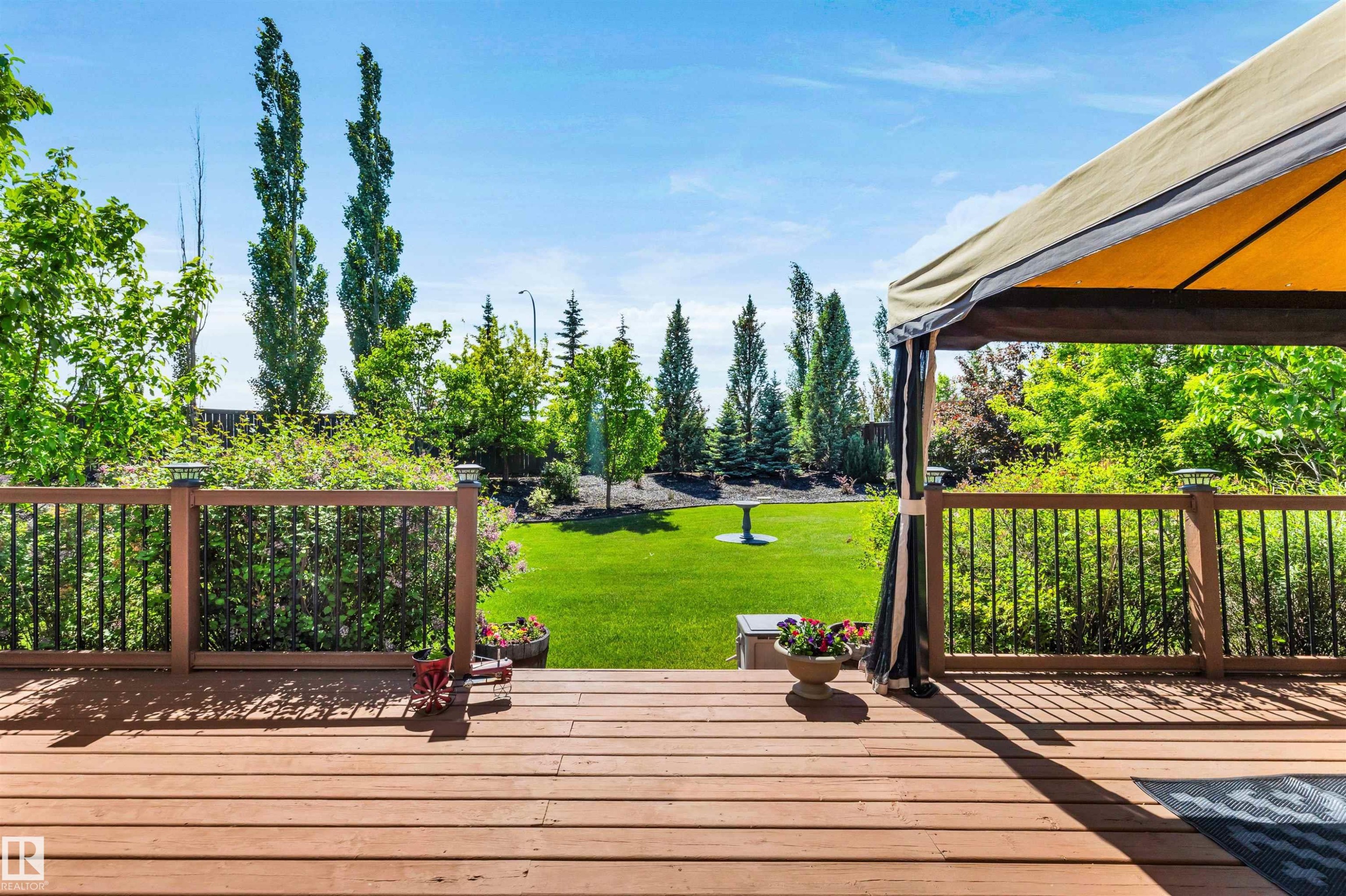 Spacious wood-finish deck with a built-in gazebo, black baluster railing, and post cap lighting - 18 Voleta Crest, Spruce Grove, AB