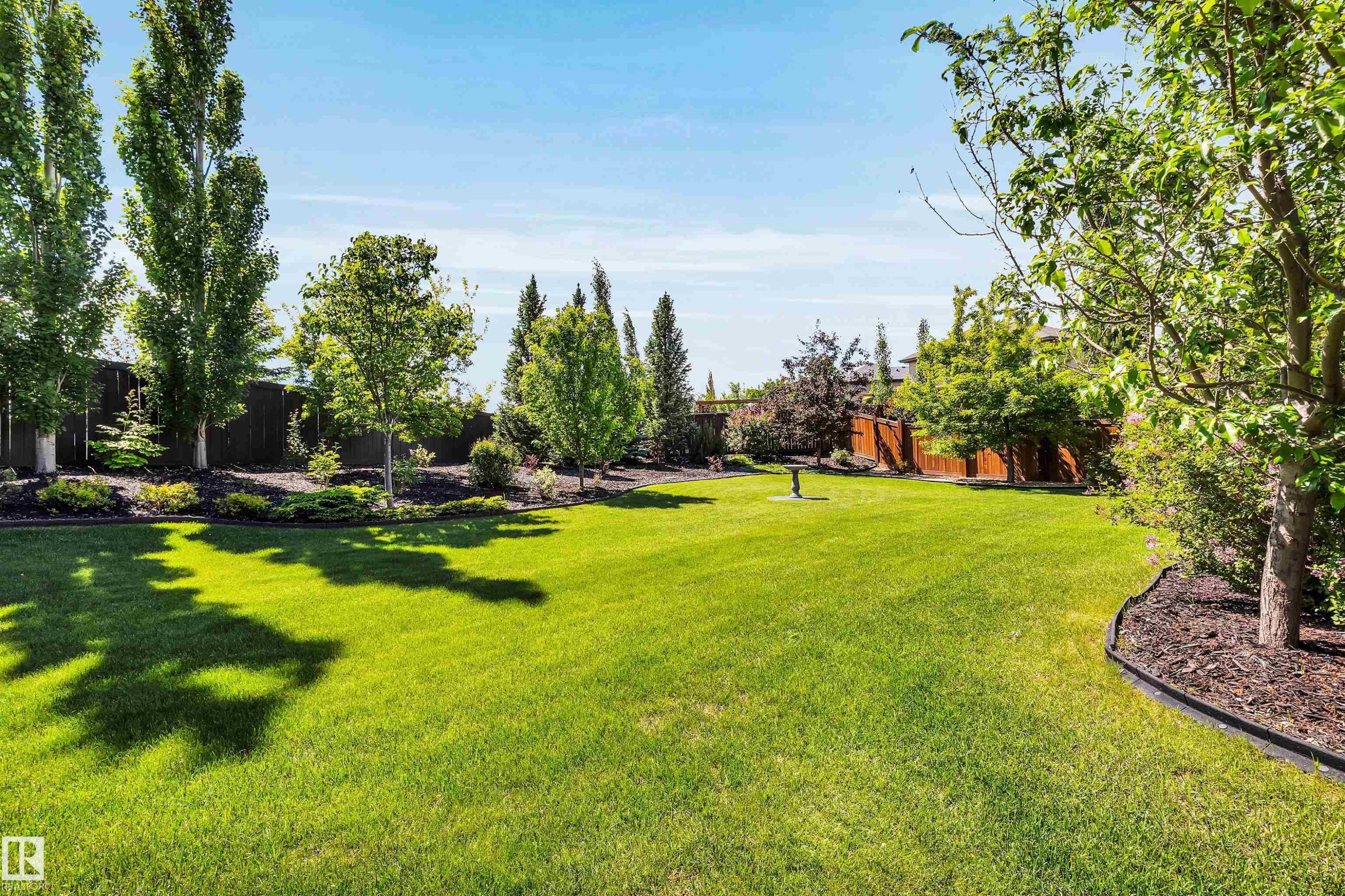Expansive backyard featuring a lush lawn, mature trees, landscaped garden beds, and a perimeter privacy fence - 18 Voleta Crest, Spruce Grove, AB