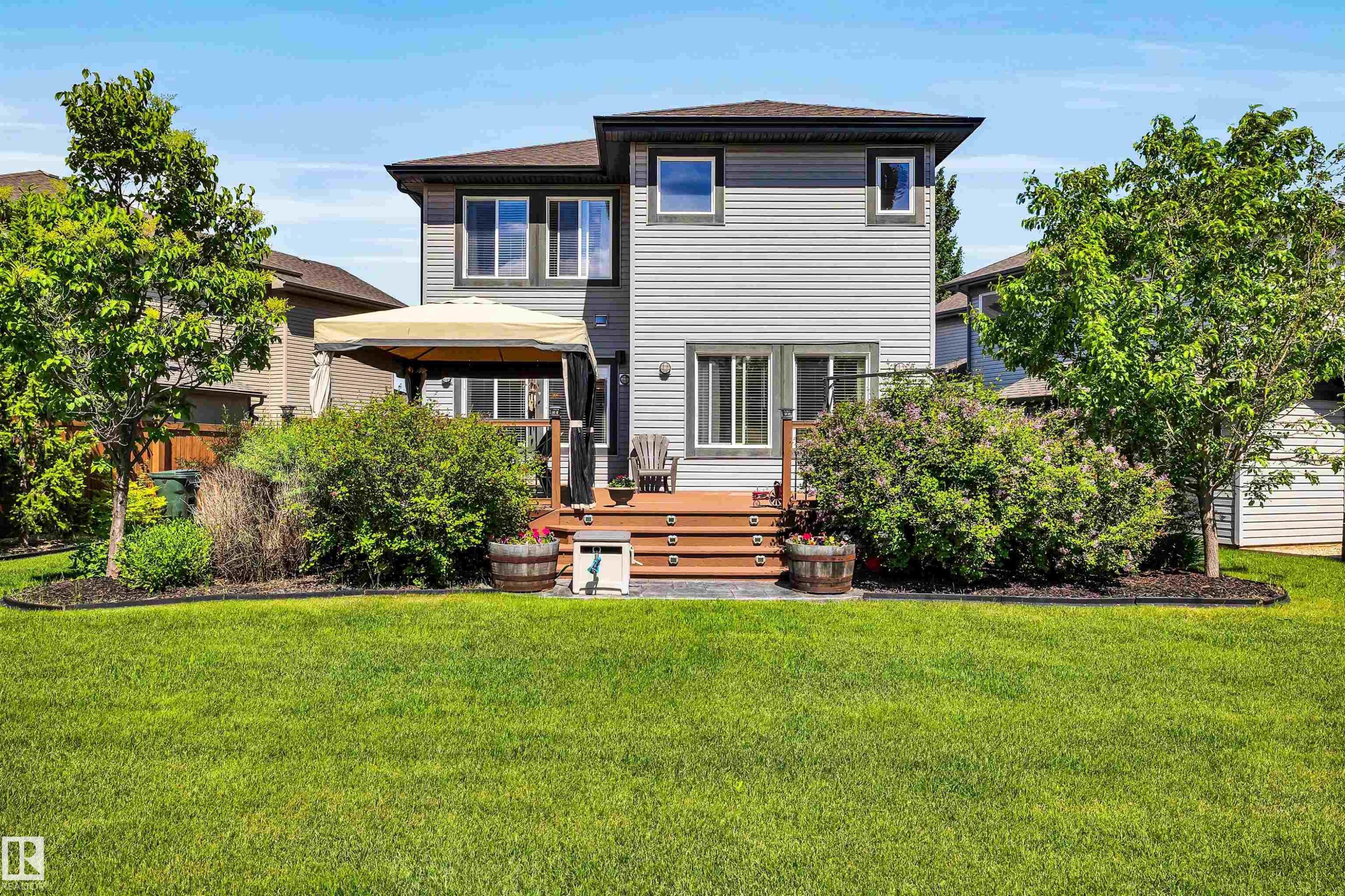 Expansive backyard featuring a manicured lawn, multi-level wood-finish deck with integrated steps, and mature perimeter landscaping - 18 Voleta Crest, Spruce Grove, AB