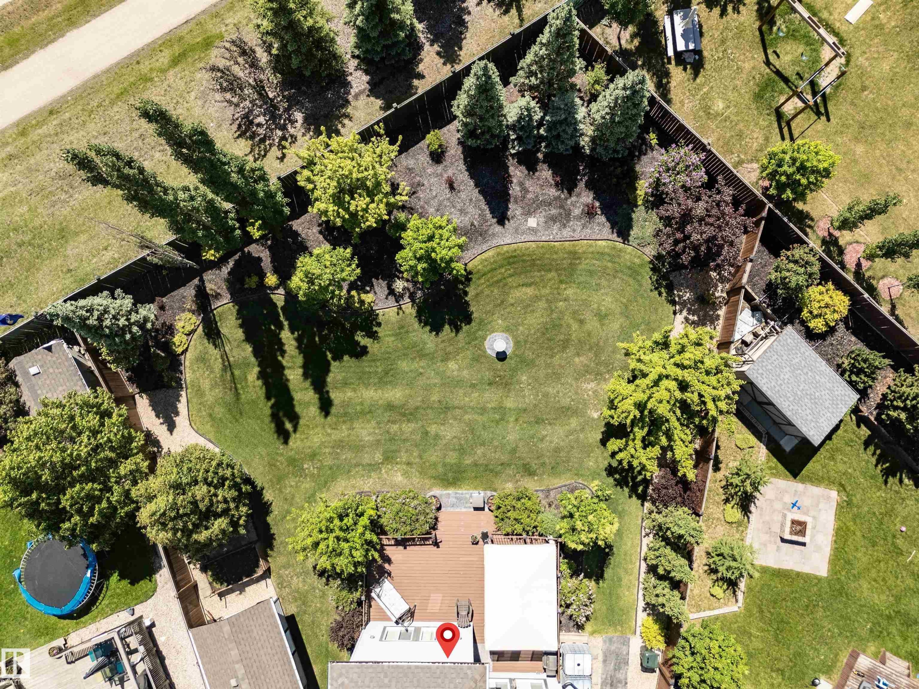 Expansive backyard featuring a large lawn, perimeter fencing, mature trees, a detached shed with a gabled roof, and a square fire pit - 18 Voleta Crest, Spruce Grove, AB