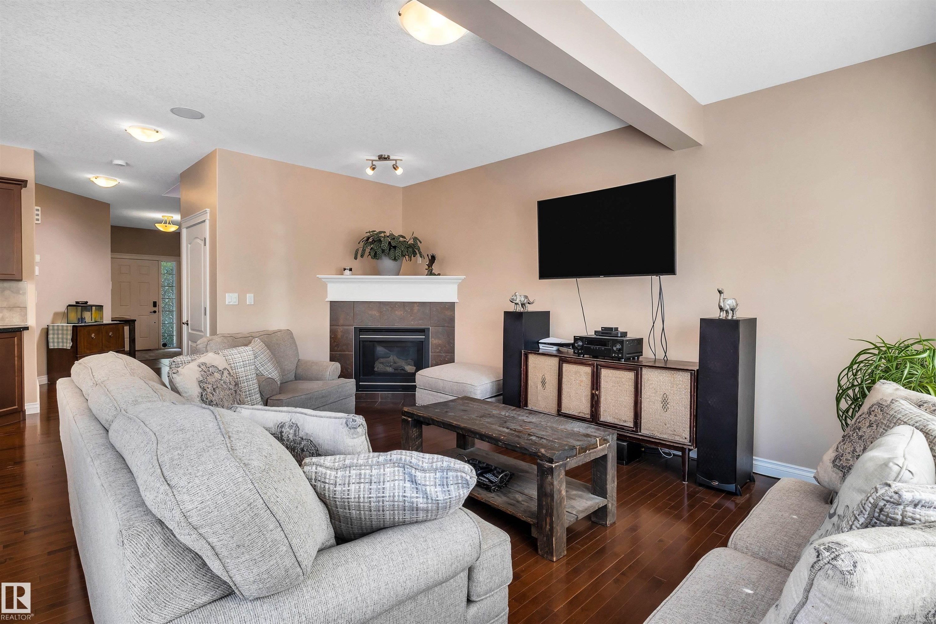 Living area featuring rich wood-finish flooring, a contemporary fireplace with a tile surround and white mantel, and ceiling-mounted light fixtures - 18 Voleta Crest, Spruce Grove, AB