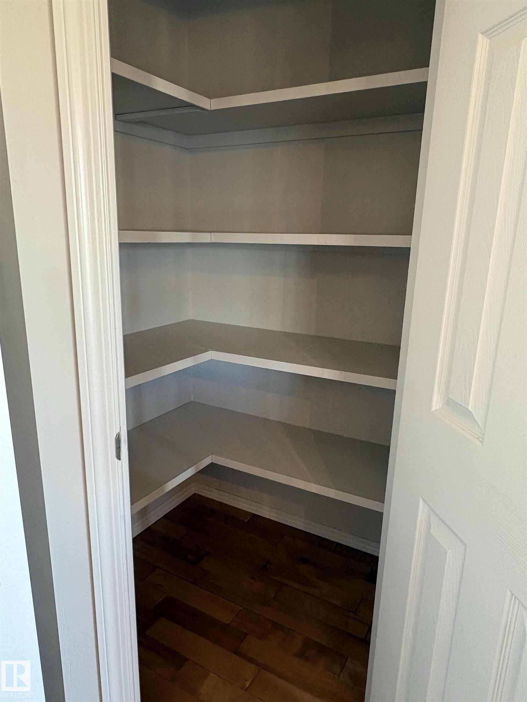 Corner pantry with multiple built-in shelves, wood-finish flooring, and white trim - 21354 87A Avenue, Edmonton, AB