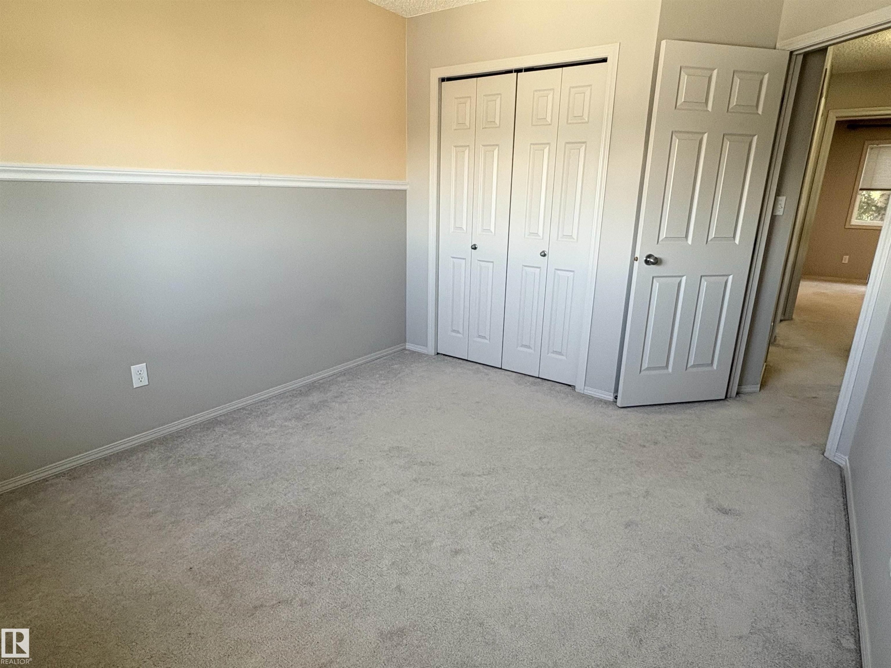 Carpeted room featuring a two-tone wall treatment with a chair rail, a bi-fold closet door, and a paneled entry door - 21354 87A Avenue, Edmonton, AB