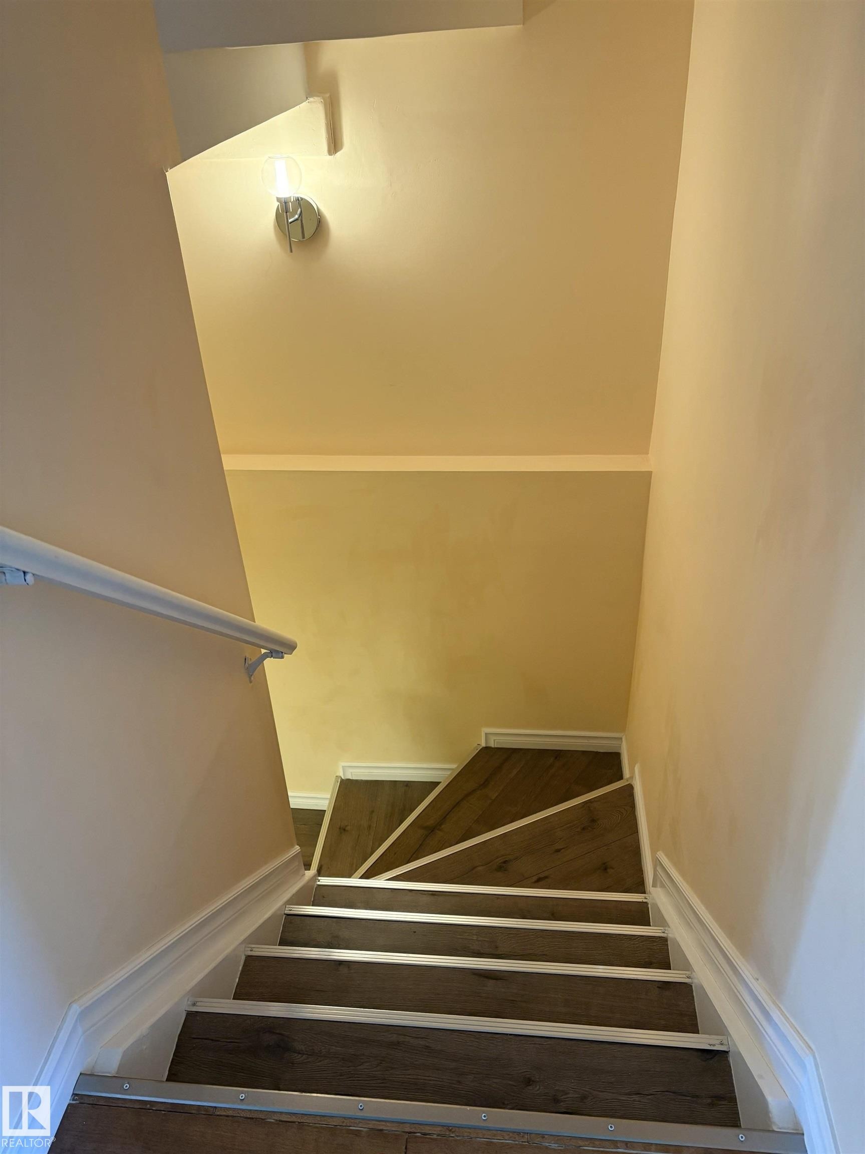 Staircase featuring wood-finish treads with silver-tone nosing, white baseboards, and a white wall-mounted handrail - 21354 87A Avenue, Edmonton, AB