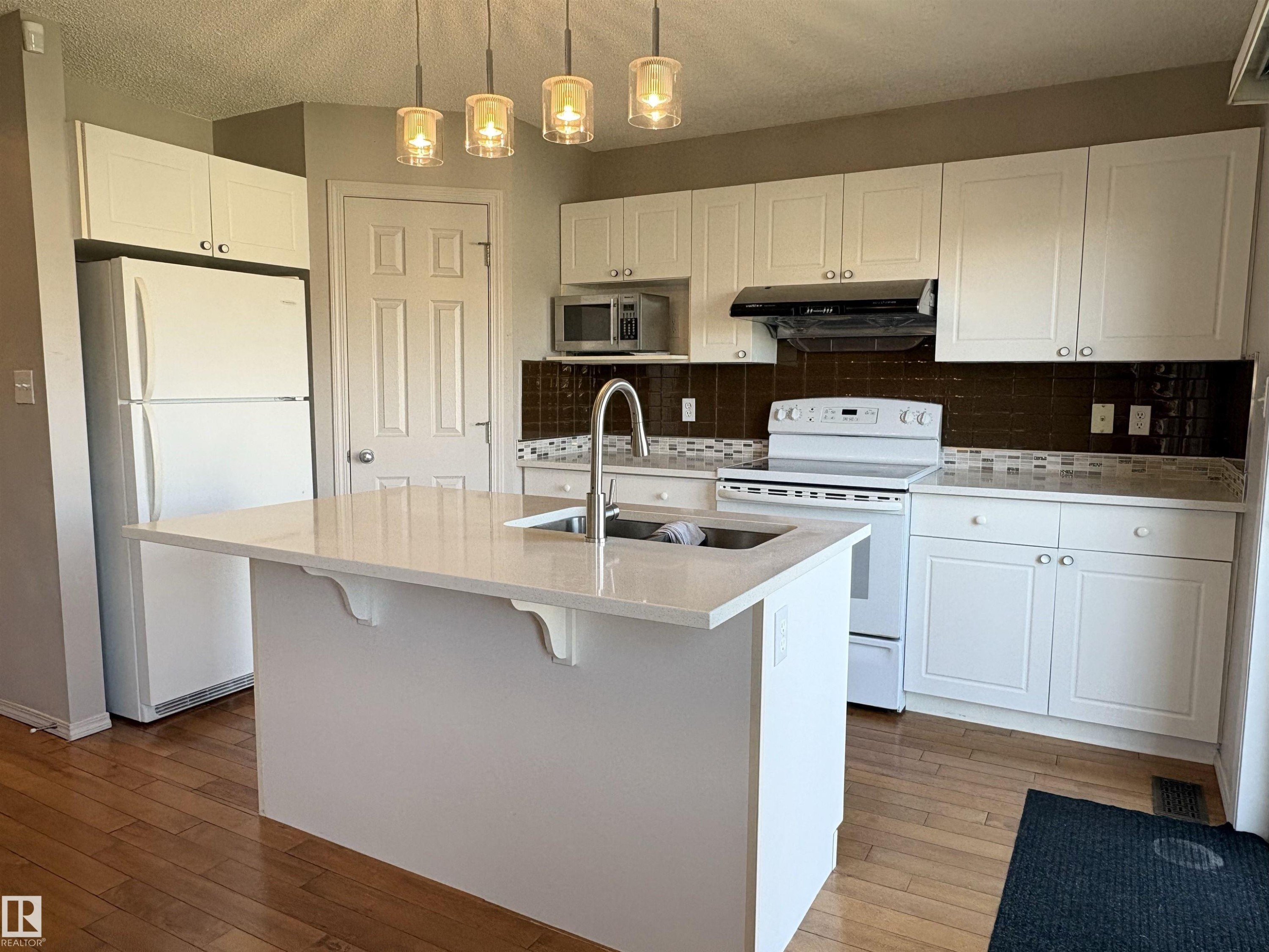 Modern kitchen featuring white cabinetry, a central island with a solid surface countertop, and wood-finish flooring - 21354 87A Avenue, Edmonton, AB