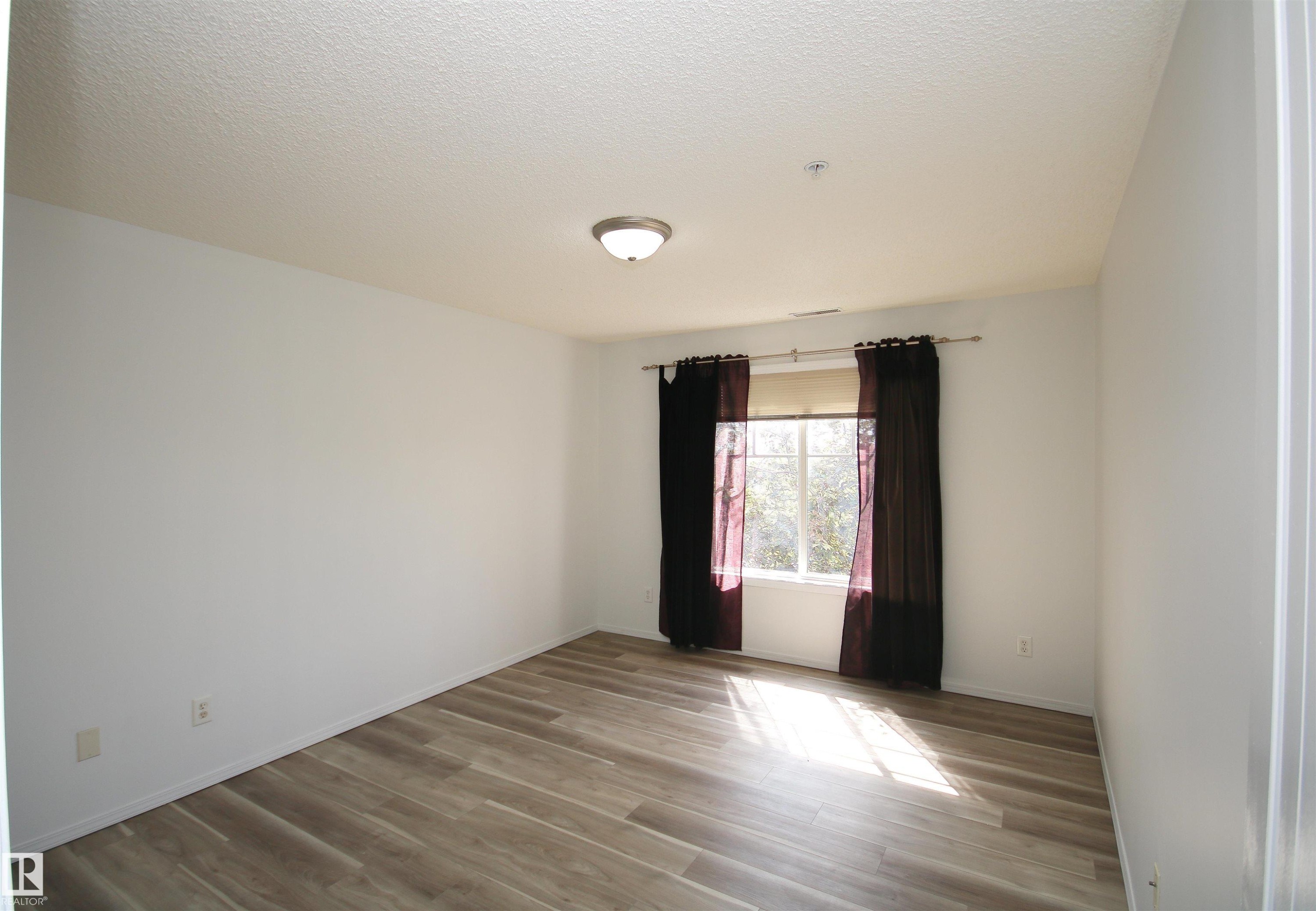 Neutral color palette room featuring wood-finish flooring, a double window with blinds, and a flush-mount ceiling light fixture - 311 2098 Blackmud Creek Drive, Edmonton, AB