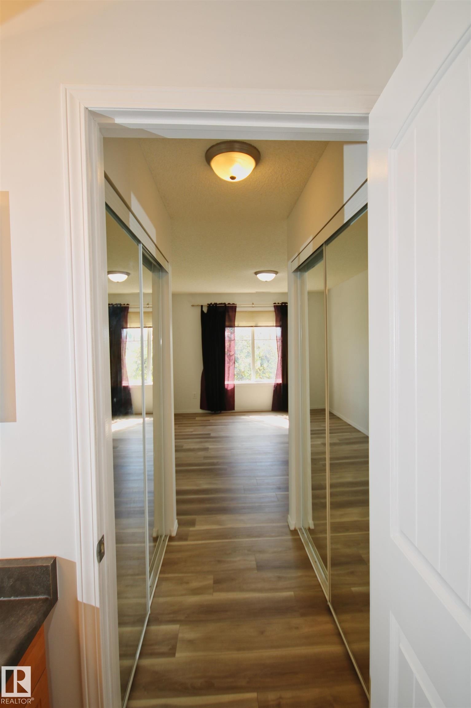 Hallway featuring wood-finish flooring, mirrored sliding closet doors, and recessed lighting - 311 2098 Blackmud Creek Drive, Edmonton, AB