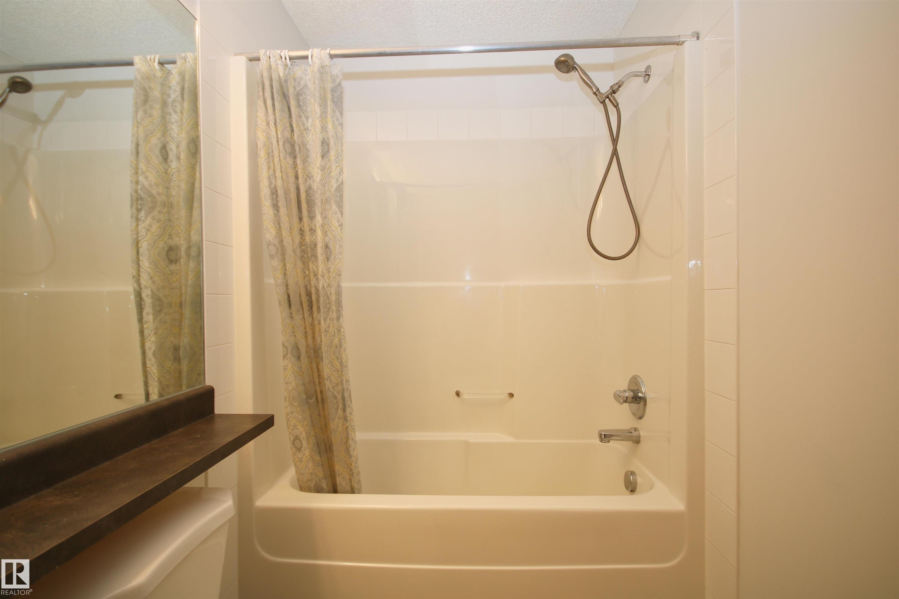 Alcove bathtub and shower combination featuring a curved shower rod, chrome fixtures, and a handheld showerhead - 311 2098 Blackmud Creek Drive, Edmonton, AB