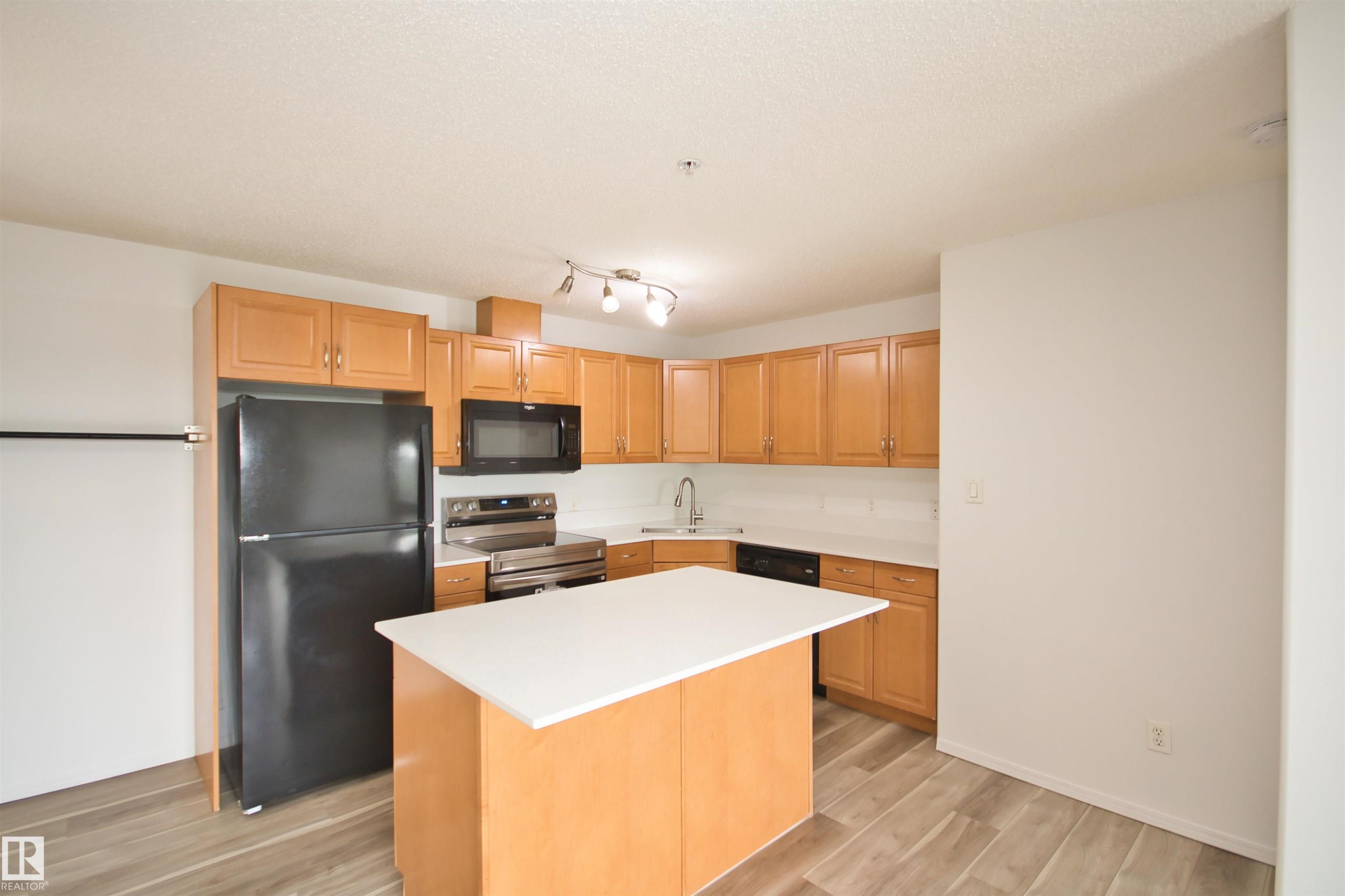 Kitchen featuring wood-finish cabinetry, white countertops, a central island, stainless steel appliances, and wood-look flooring - 311 2098 Blackmud Creek Drive, Edmonton, AB