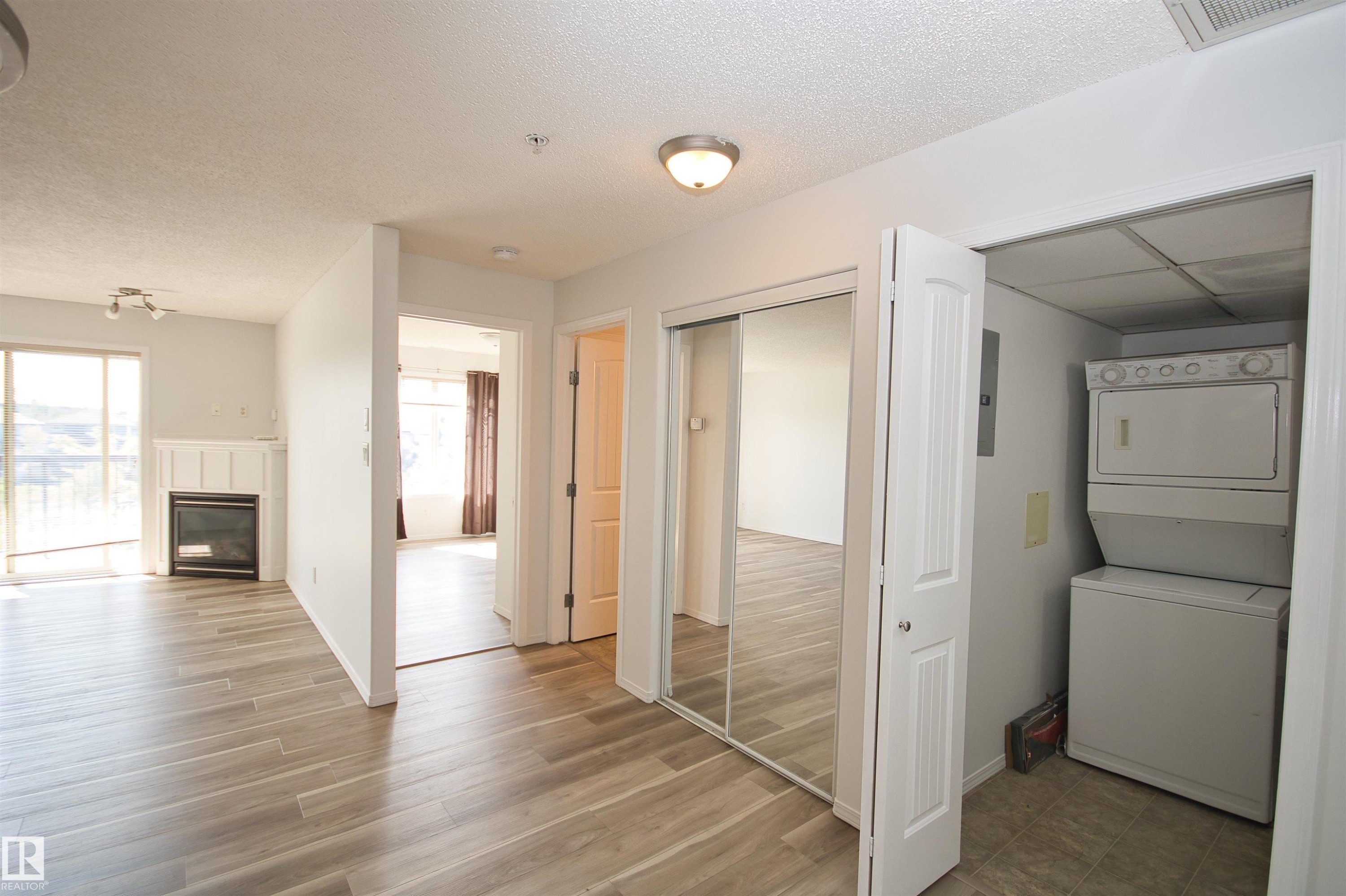 Light wood-finish flooring throughout, featuring a fireplace with white mantel, sliding glass door, mirrored closet doors, and built-in laundry appliances - 311 2098 Blackmud Creek Drive, Edmonton, AB