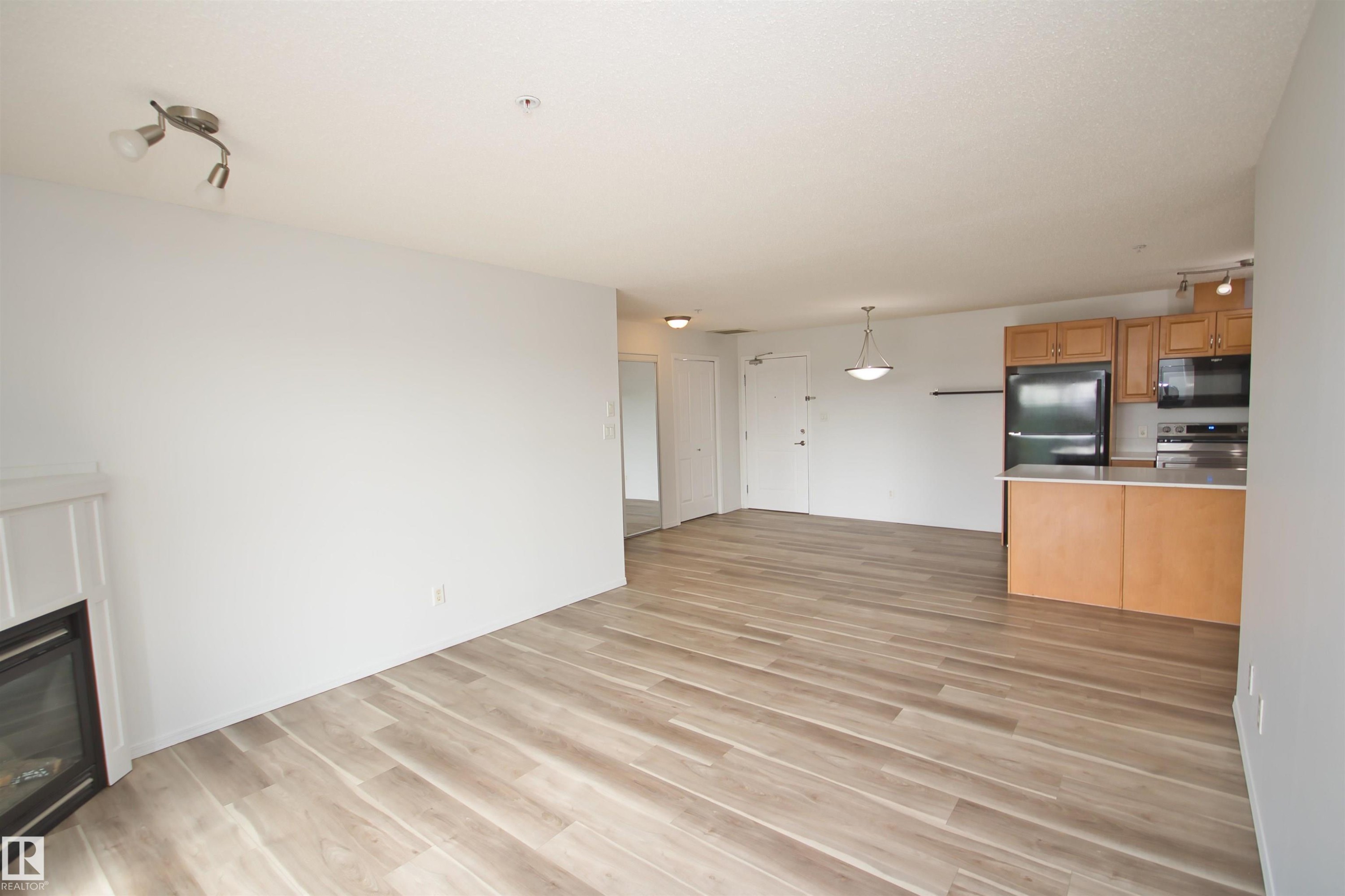Open-concept living area with wood-finish flooring, a contemporary fireplace, and recessed lighting - 311 2098 Blackmud Creek Drive, Edmonton, AB